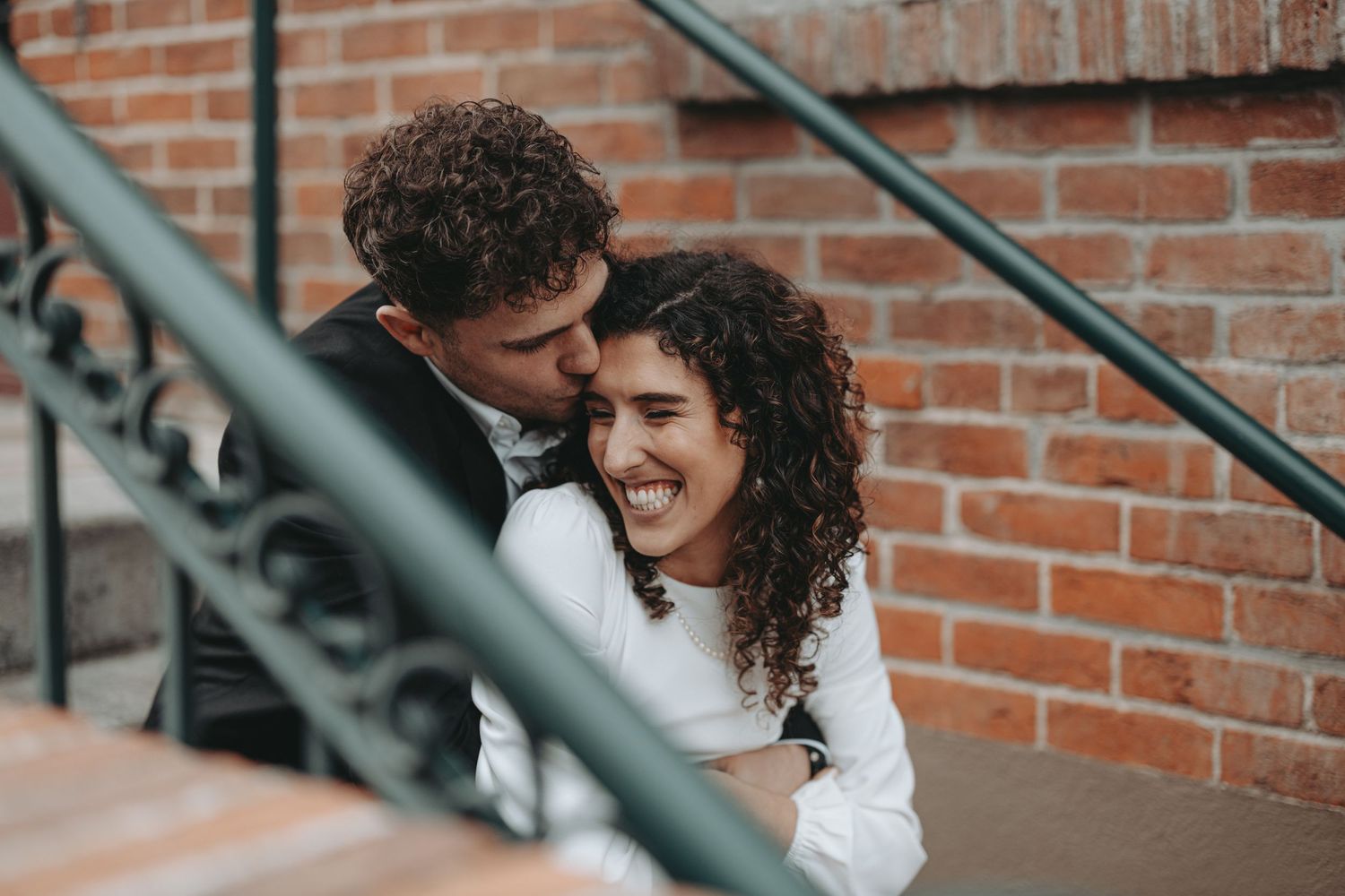 A romantic couple embracing on brick steps with bride in white and groom in dark suit.