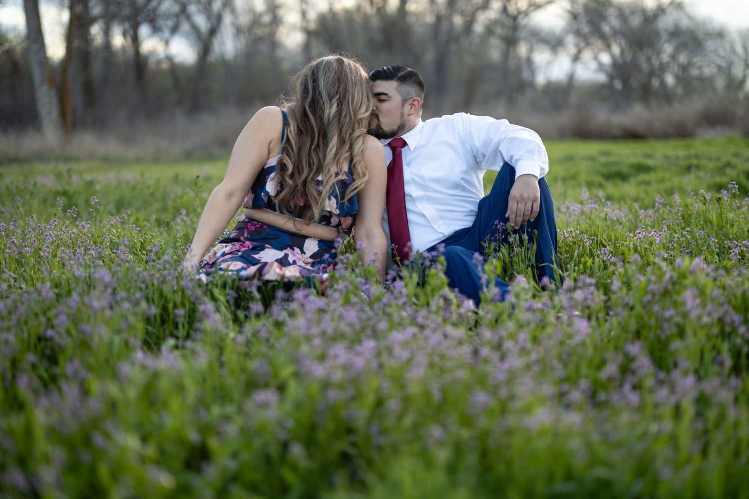 A couple shares an intimate moment while sitting in a field of purple wildflowers at dusk.