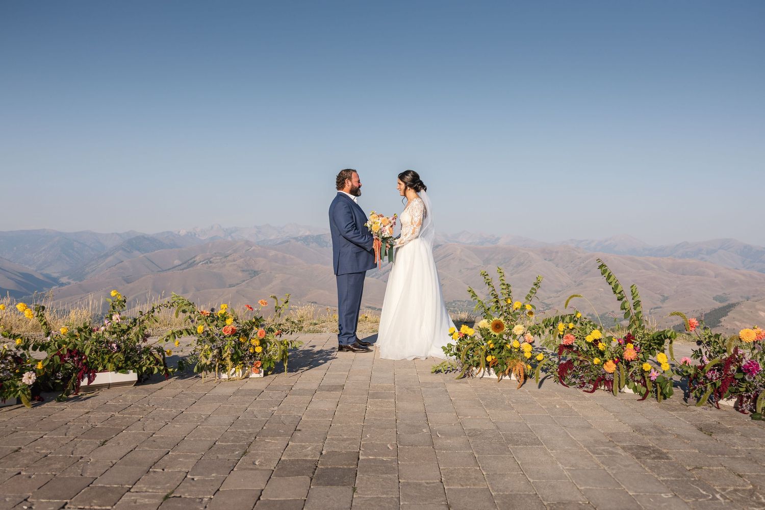 Wedding ceremony setup on a mountain peak with colorful floral arrangements and stone paved platform.