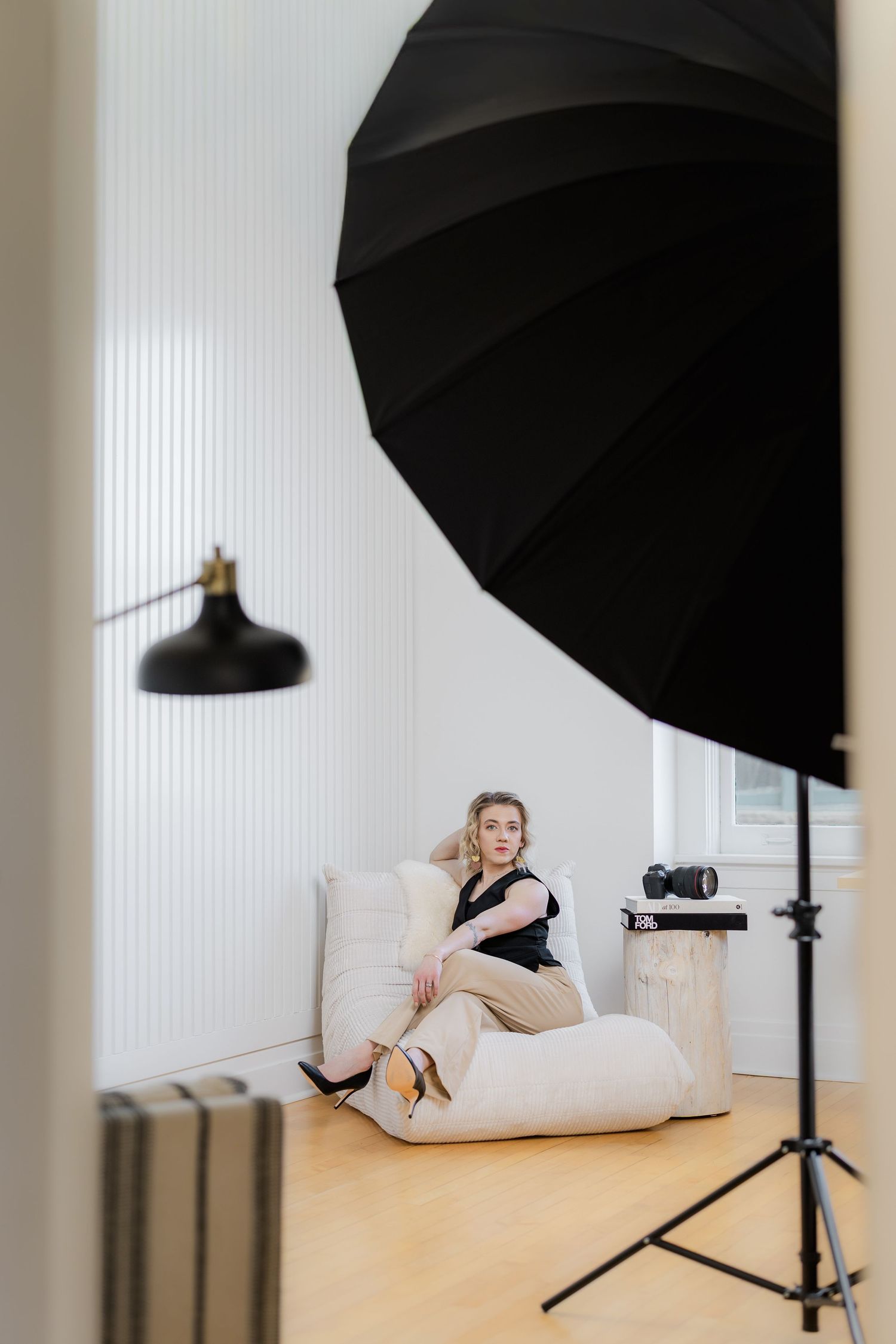 Studio photography setup showing lighting umbrellas and white backdrop with models posing on white furniture.