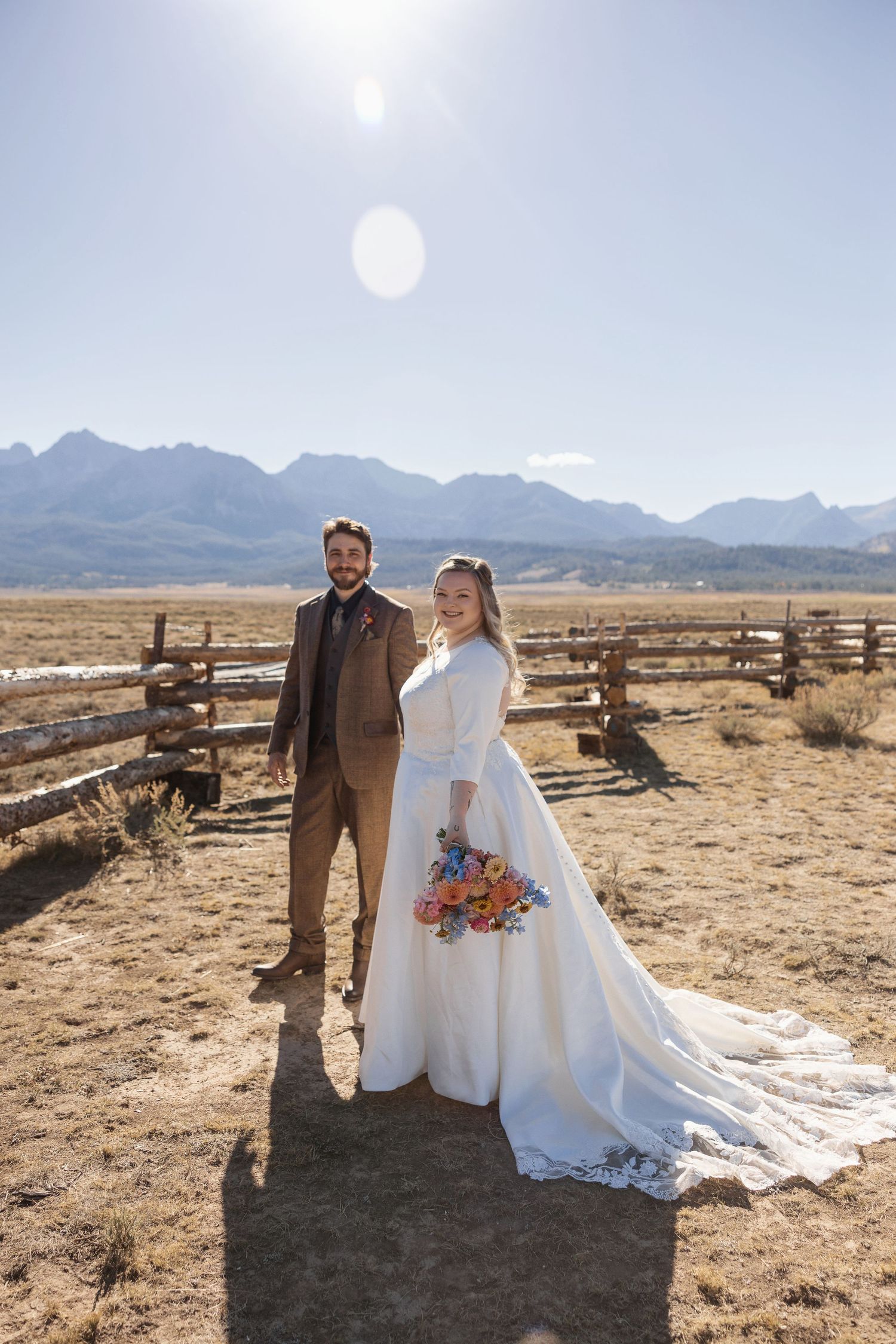 A rustic outdoor wedding scene with wooden fences and mountain landscapes in the background.