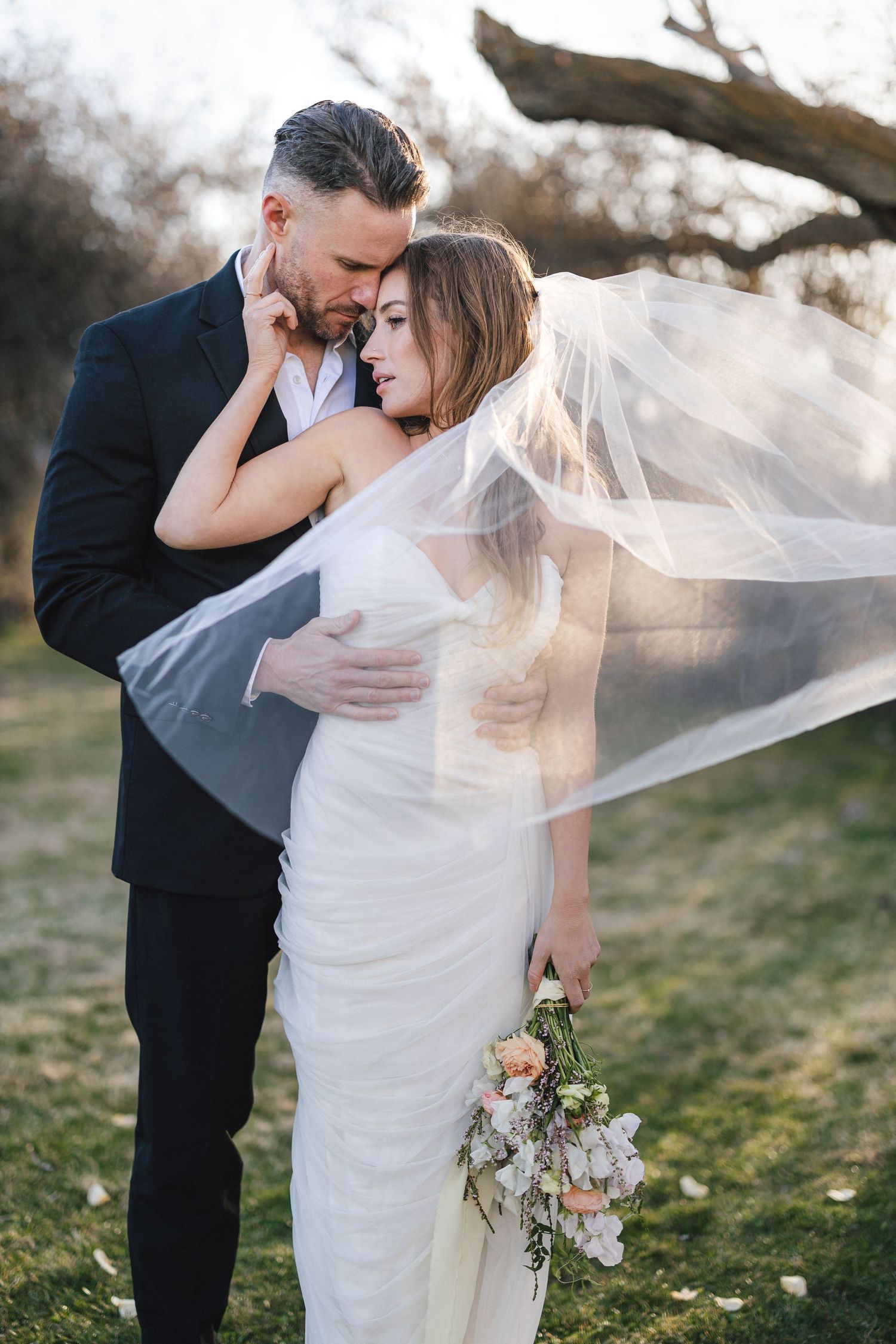 Intimate wedding portraits with flowing veil against natural outdoor backdrop.