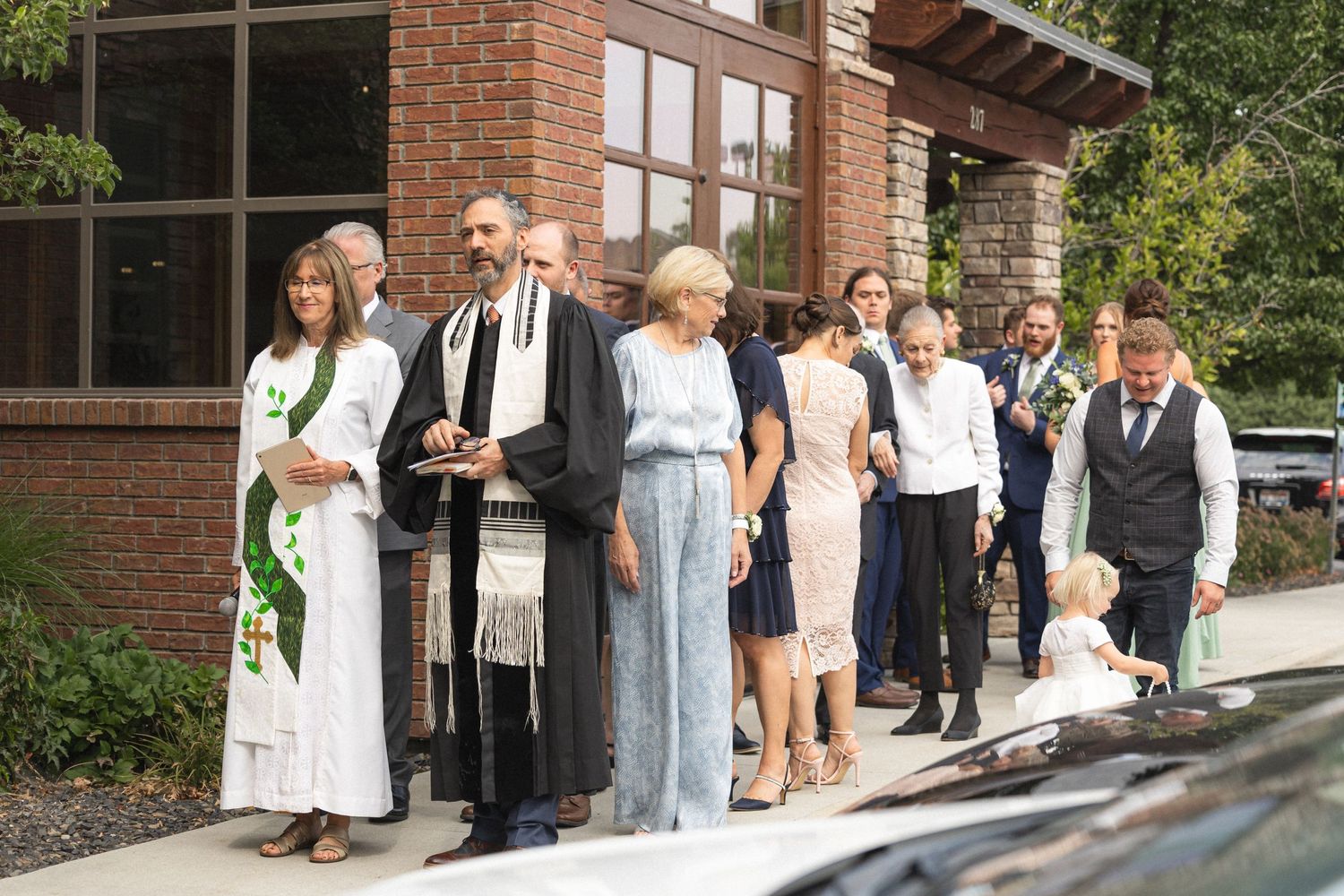Wedding guests lined up outside brick building for ceremony or reception.