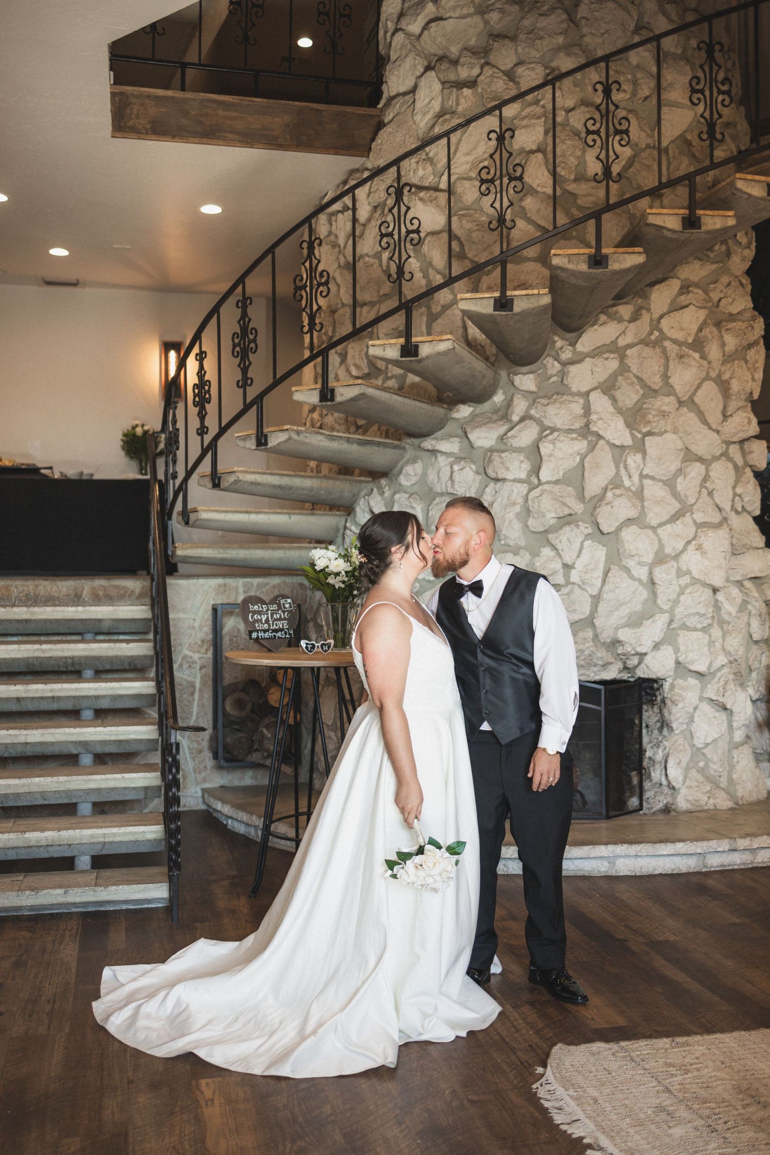A romantic moment captured by a stone staircase at an elegant indoor wedding venue.