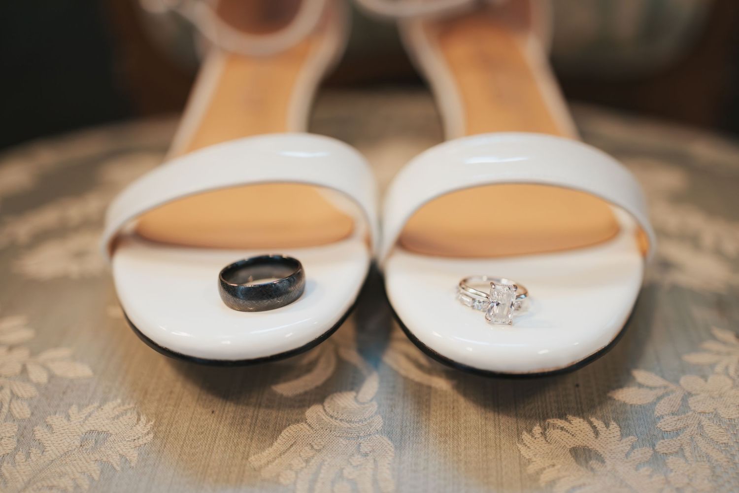 Wedding rings photographed on white bridal sandals against textured fabric.