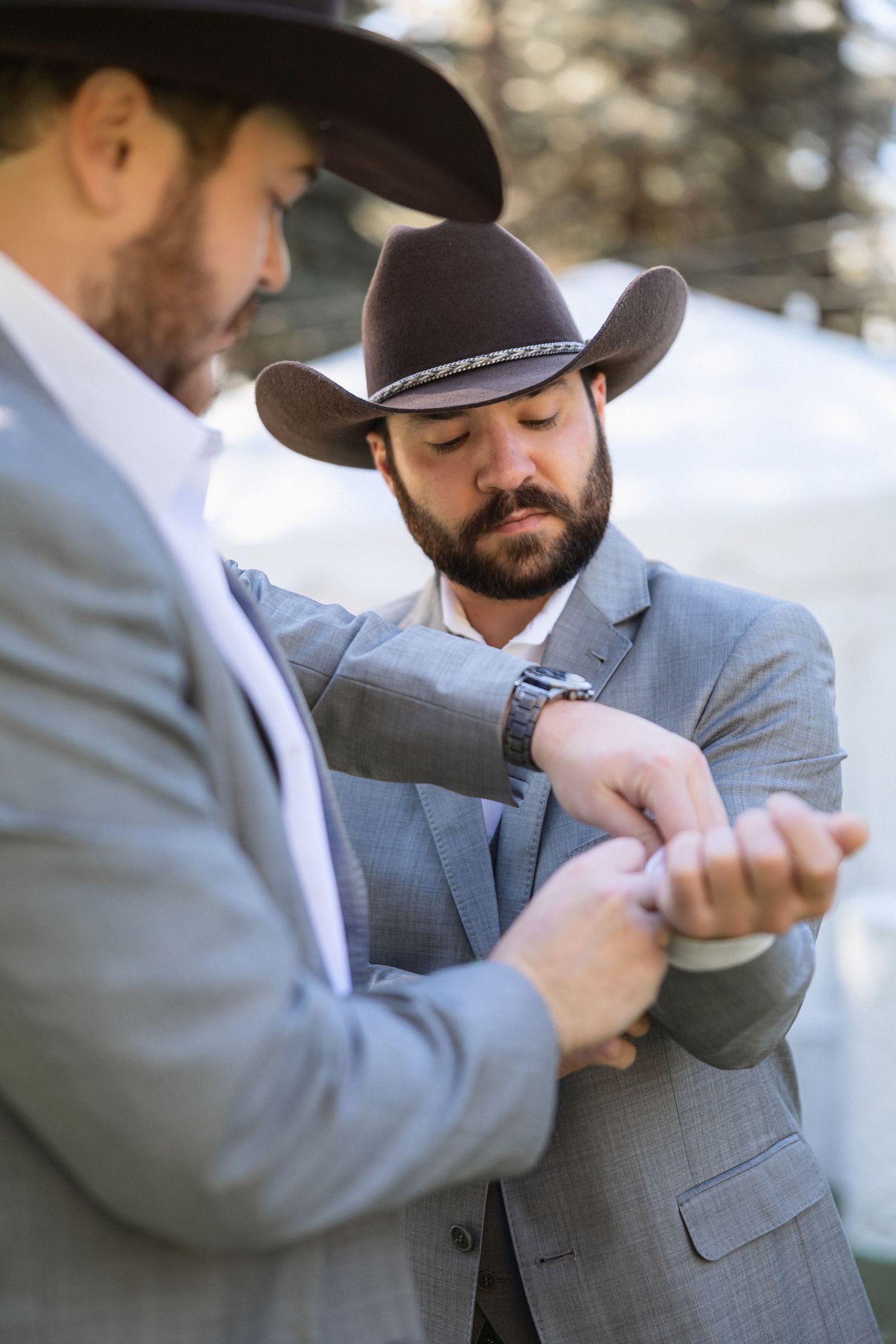 Two men in cowboy hats and grey suits examining watches or cuffs.