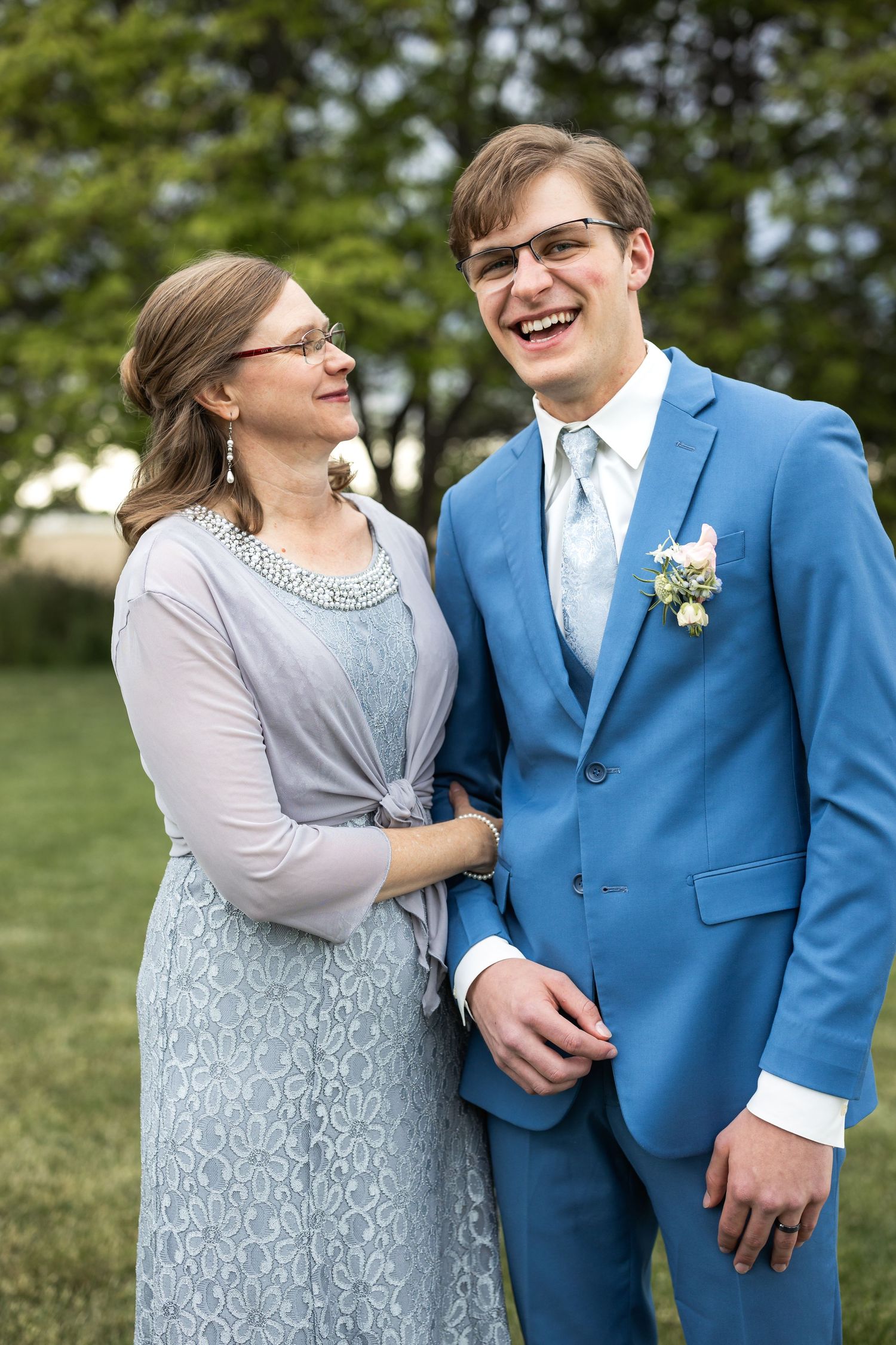 Sweet moment between groom in blue suit and wedding guest in grey lace dress.