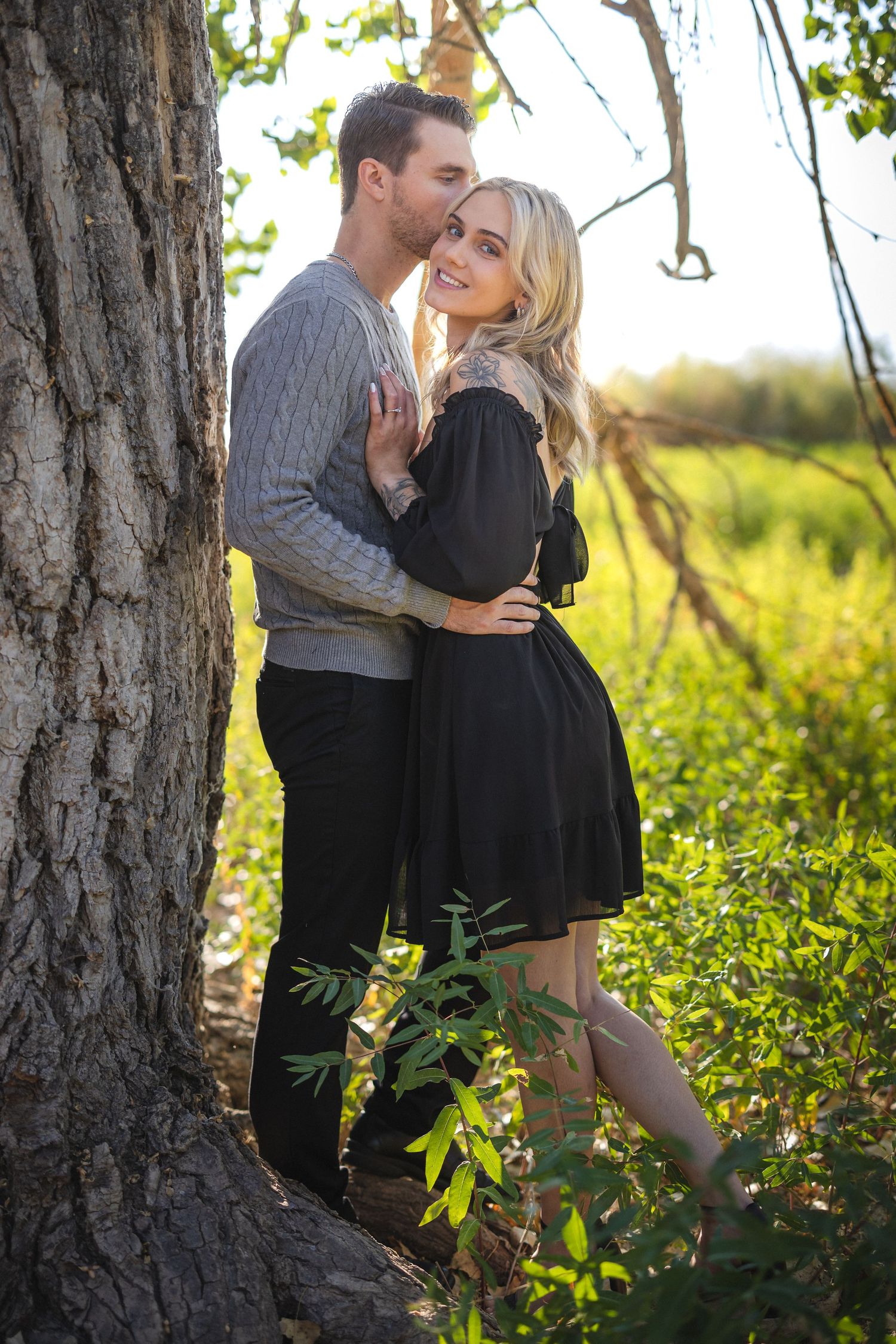 Loving couple poses against tree trunk in romantic outdoor setting.