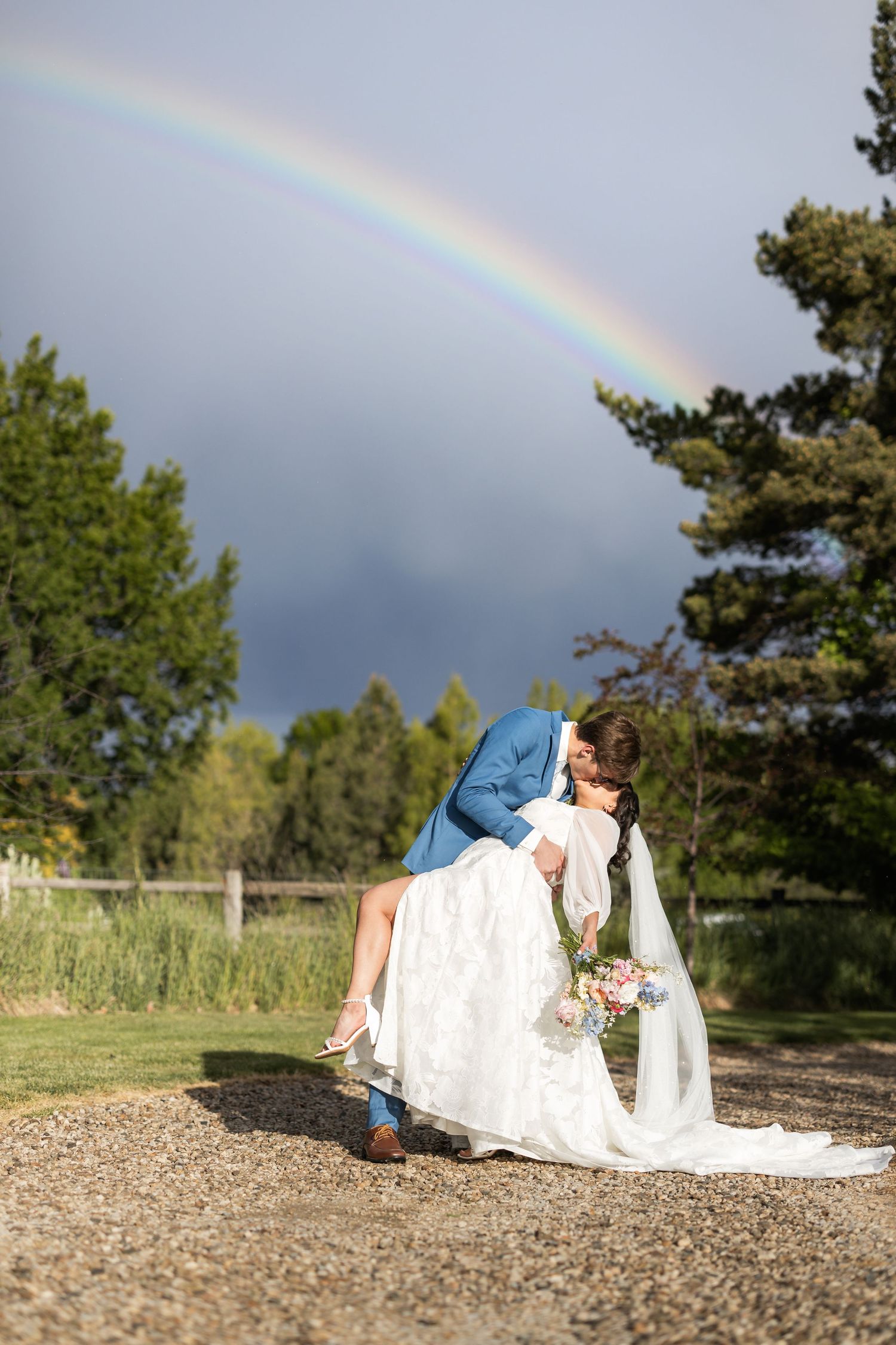 A beautiful rainbow arches across the sky during an outdoor wedding photoshoot.