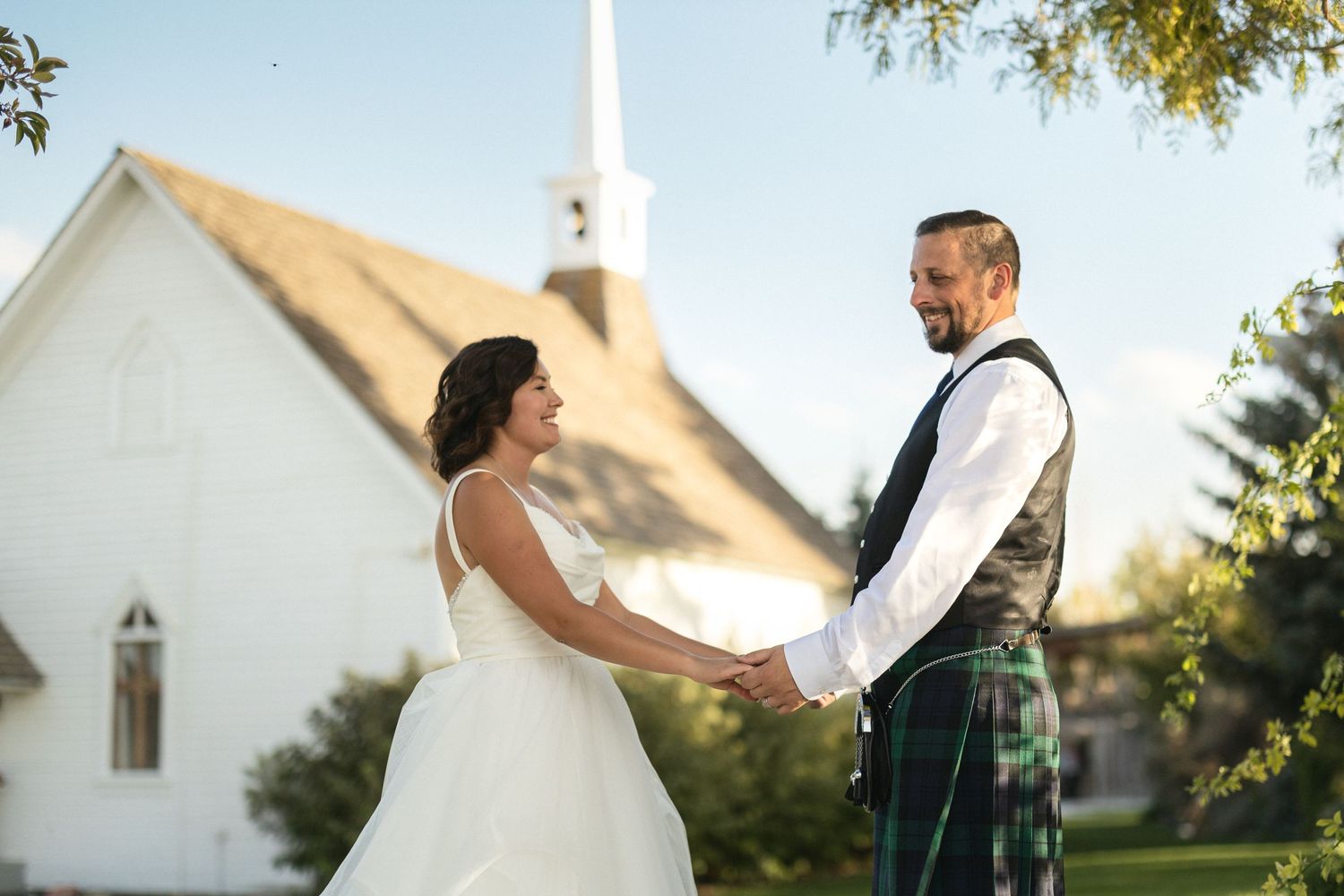 A couple shares a joyful moment outside a white church during their wedding celebration.