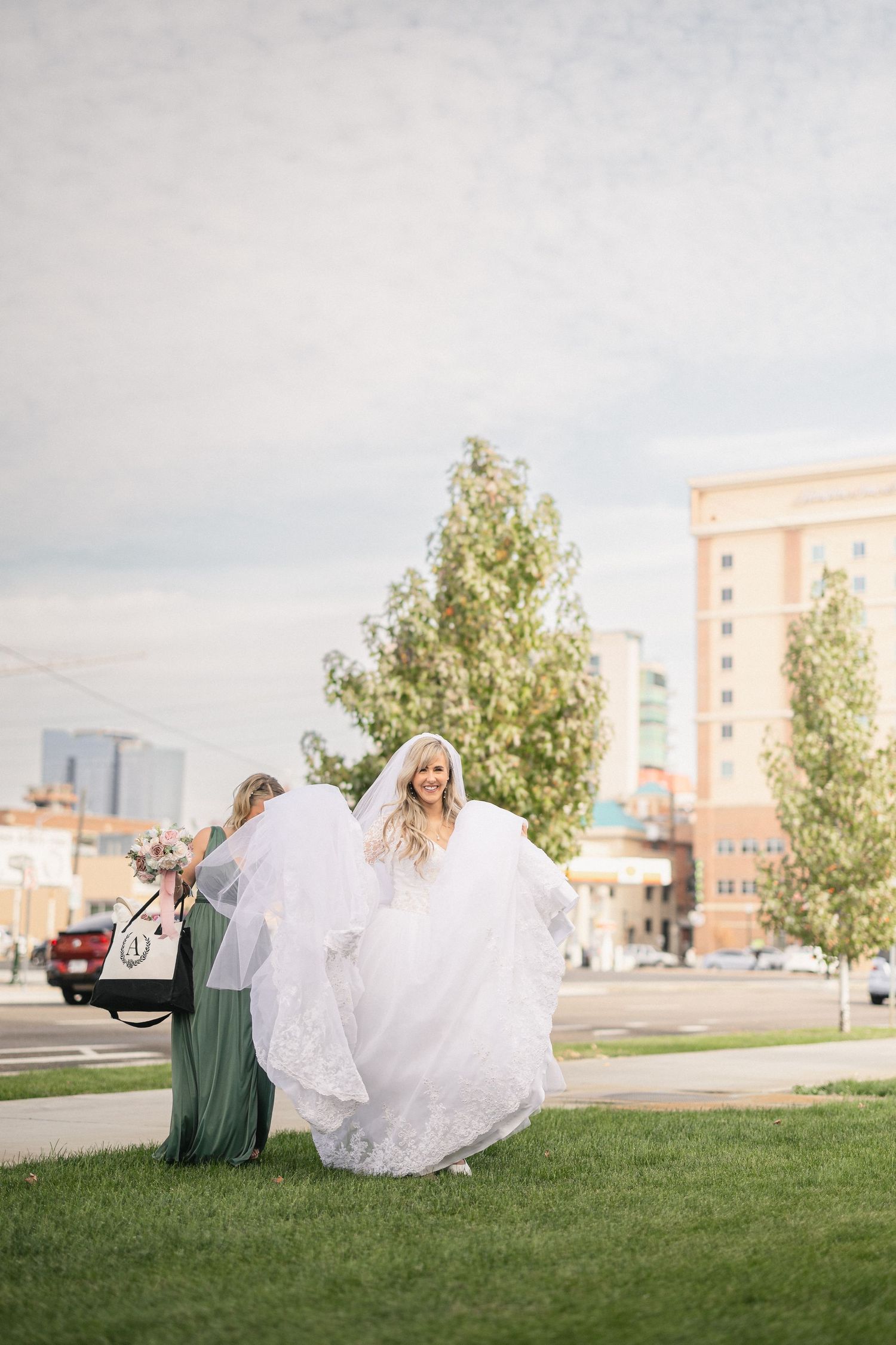 Bride in flowing white gown twirling outdoors with bridesmaid on grass.