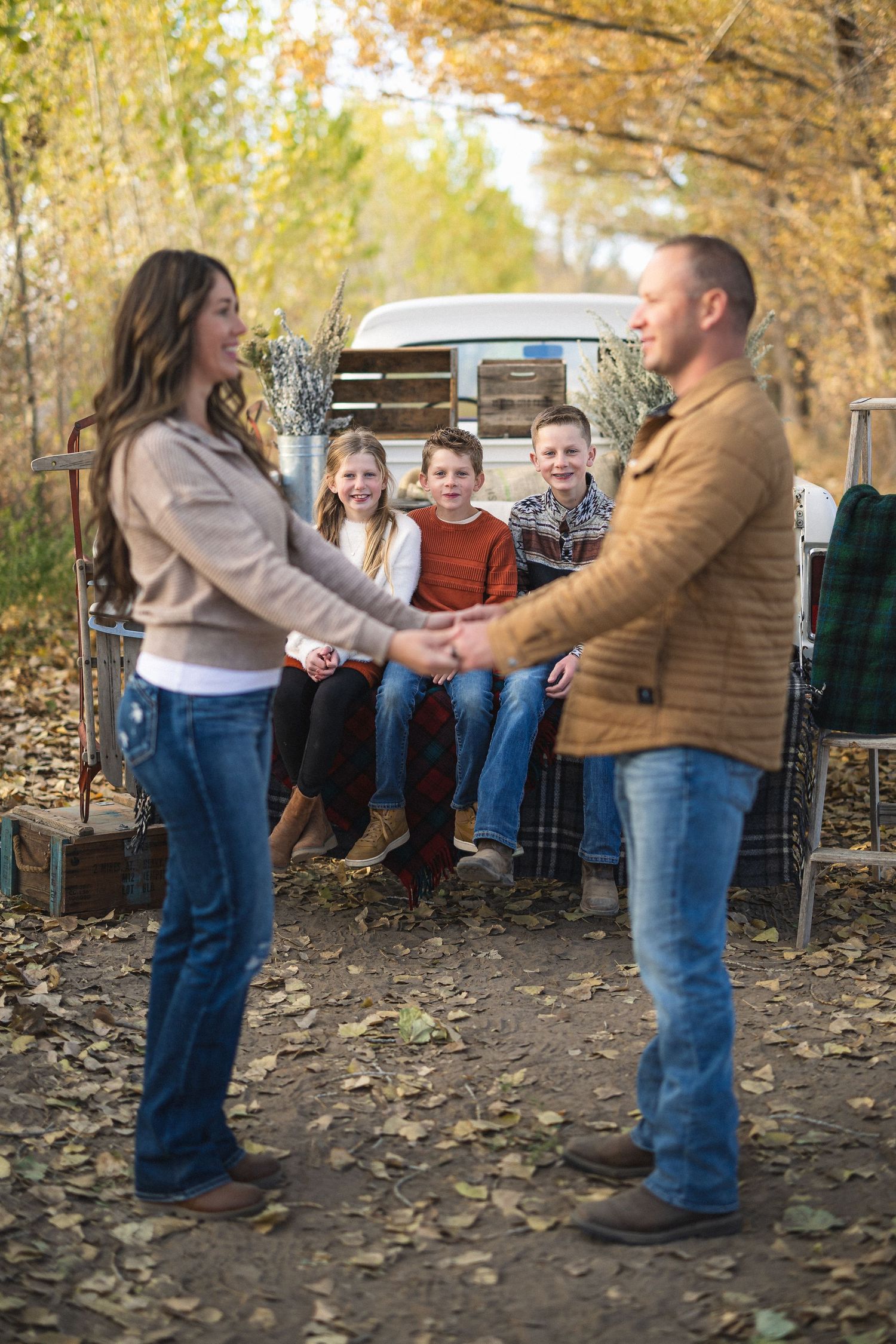Family gathering outdoors in autumn with fallen leaves and rustic bench setting.