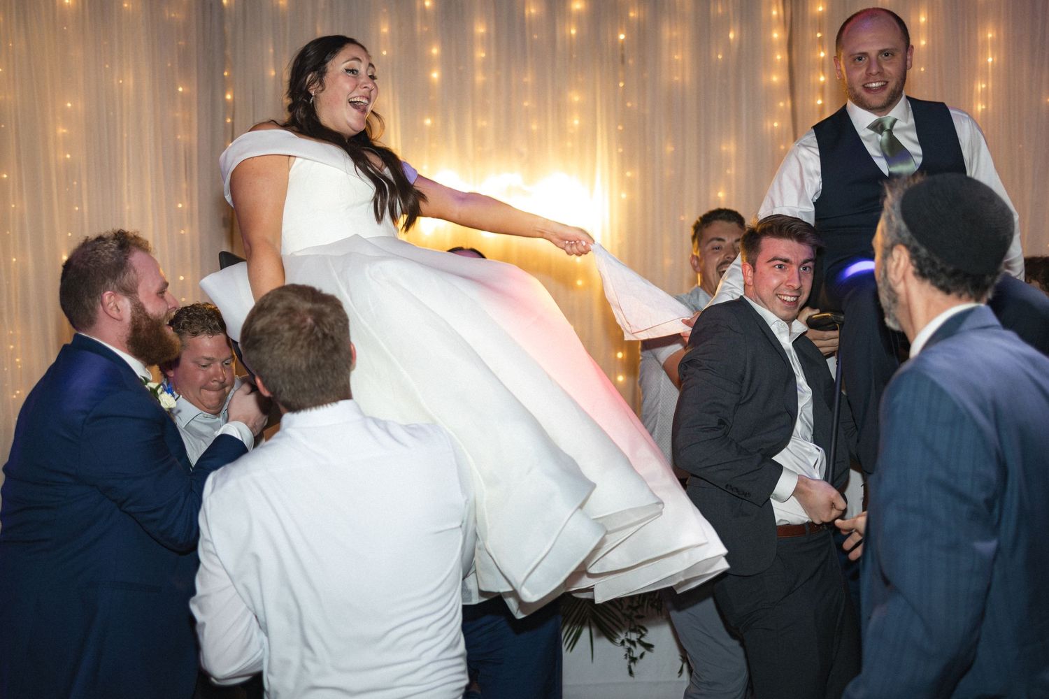 Wedding guests lift the bride in a white gown during a celebratory moment on the dance floor.