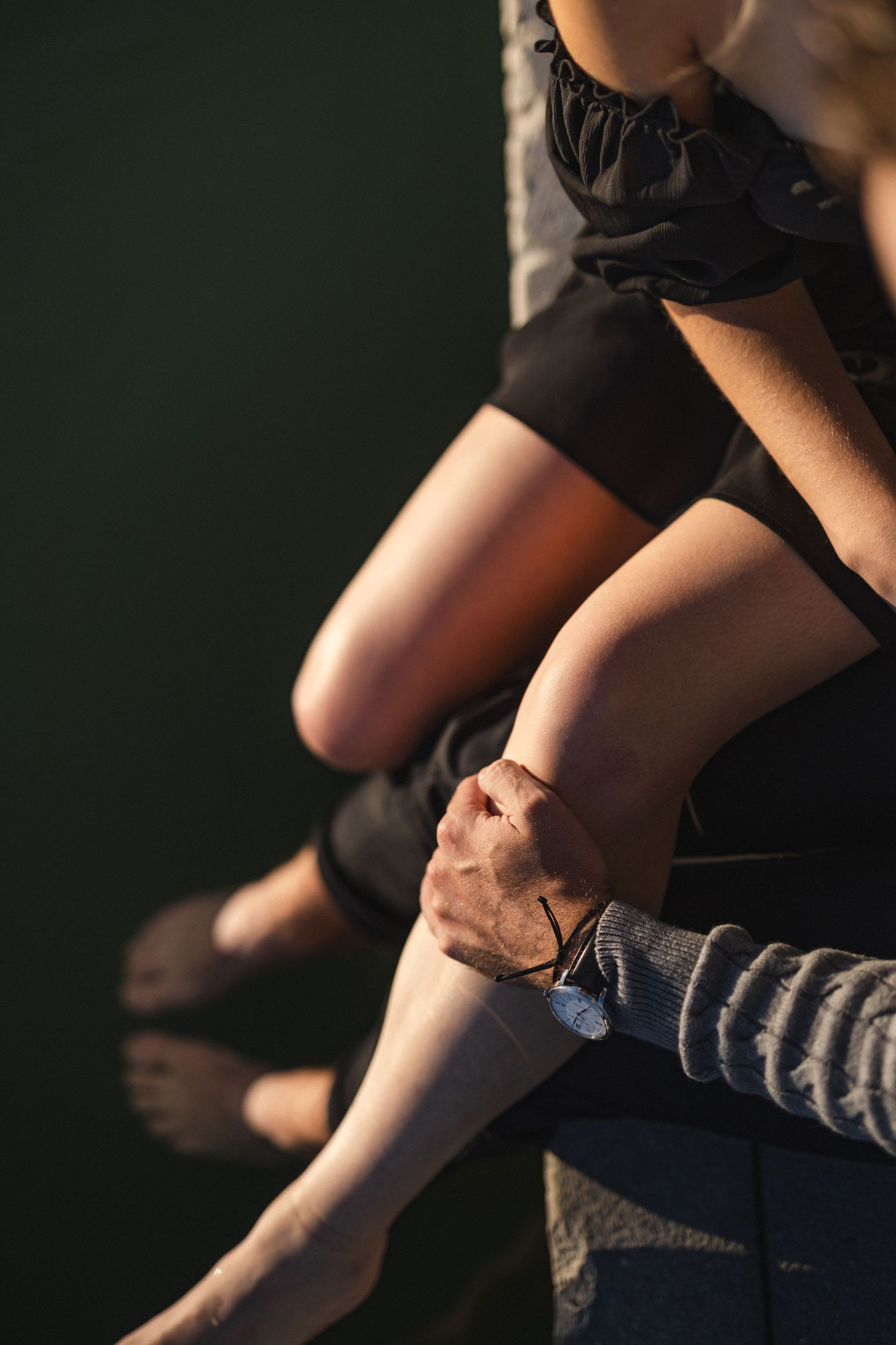 Close-up shot of bare legs dangling over water's edge in warm lighting.