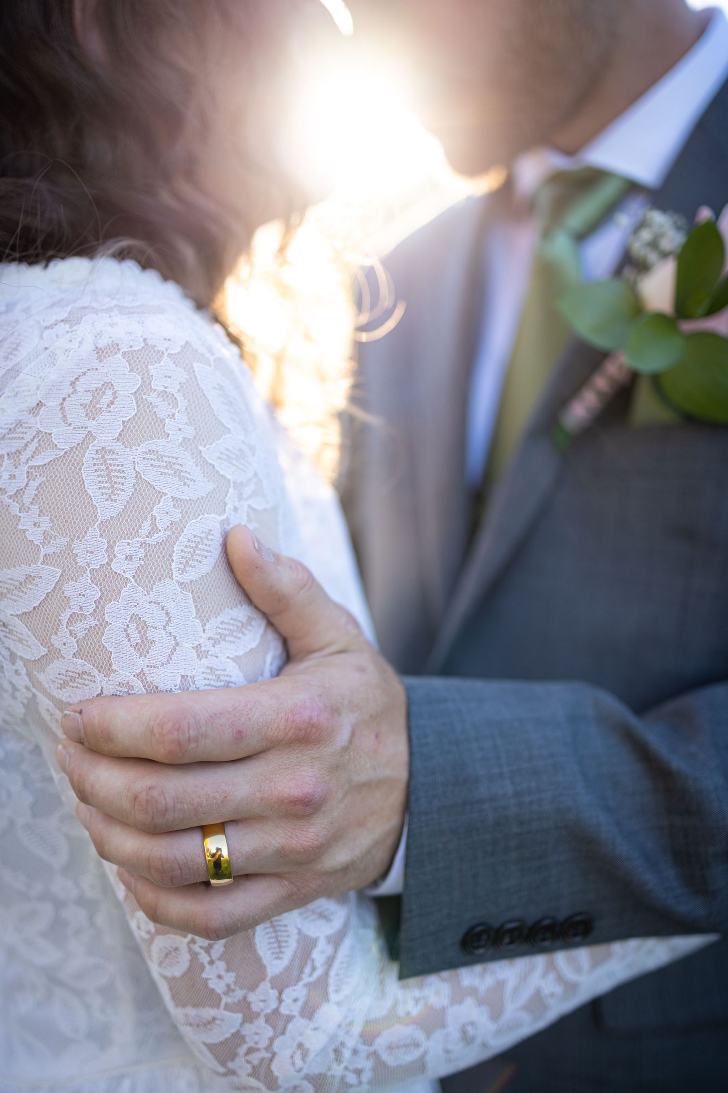 Close up of lace wedding dress detail and gold ring in sunlight.