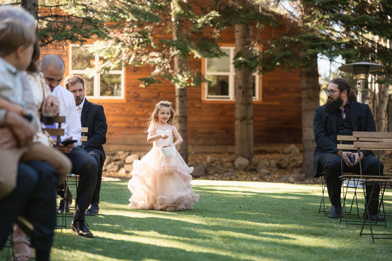 Young flower girl in pink tulle dress at outdoor wedding ceremony.