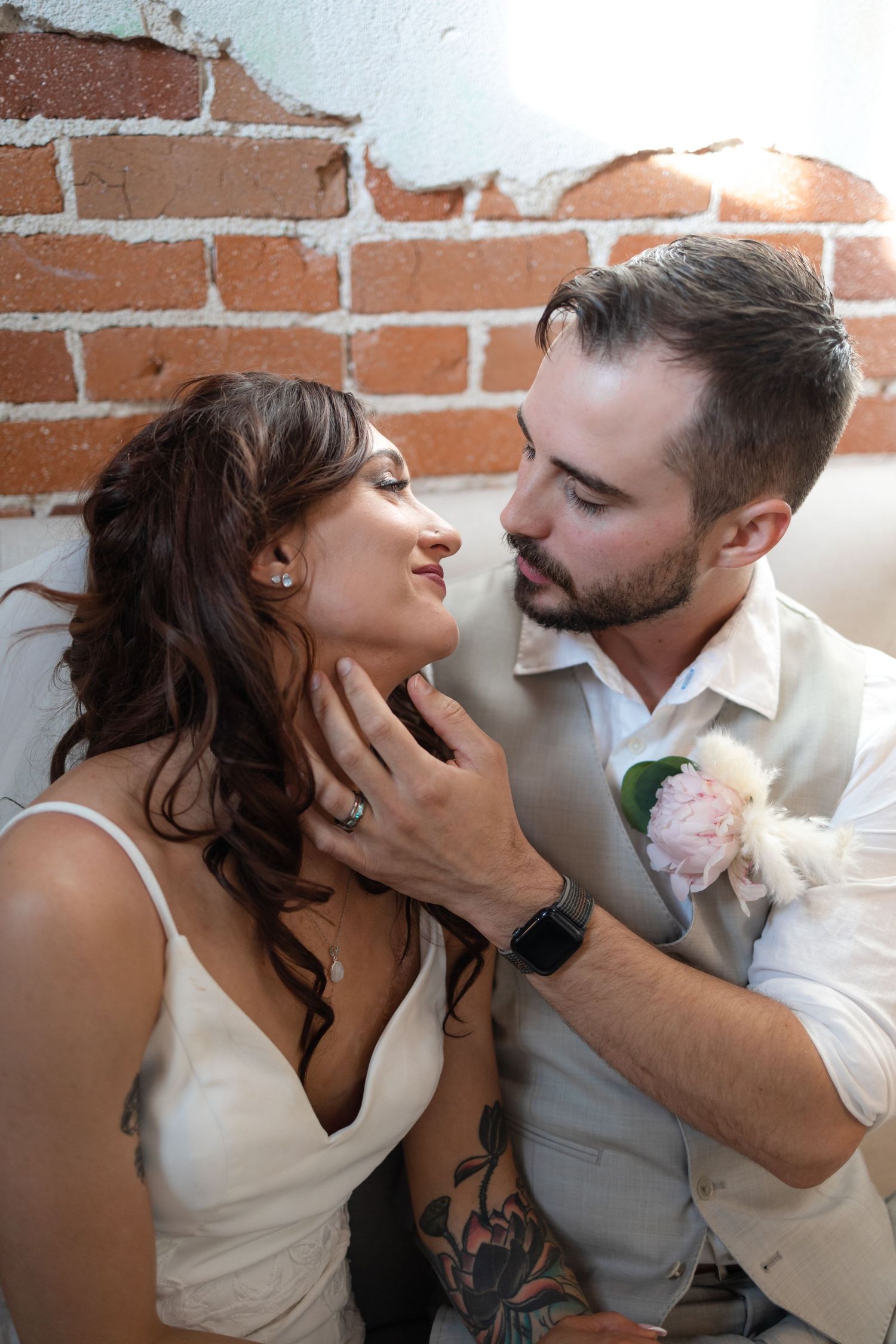 Intimate moment between bride and groom against rustic brick wall background.