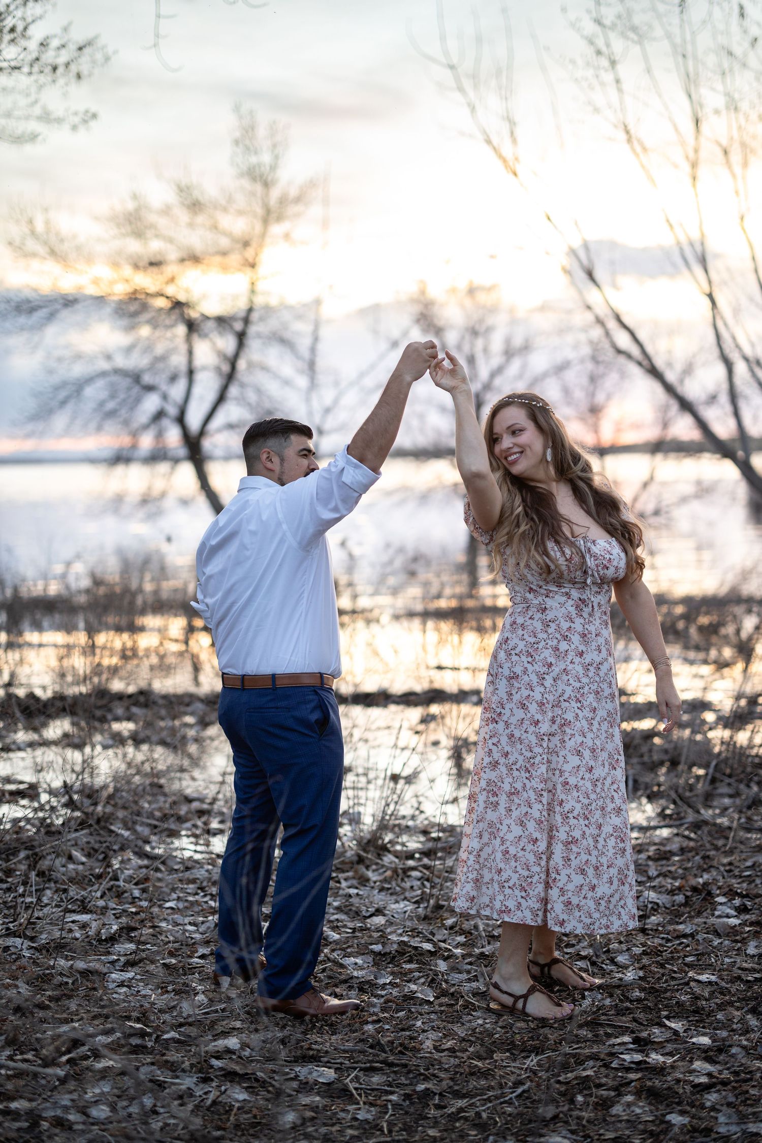 A couple dances and twirls together during a sunset photoshoot by the water.