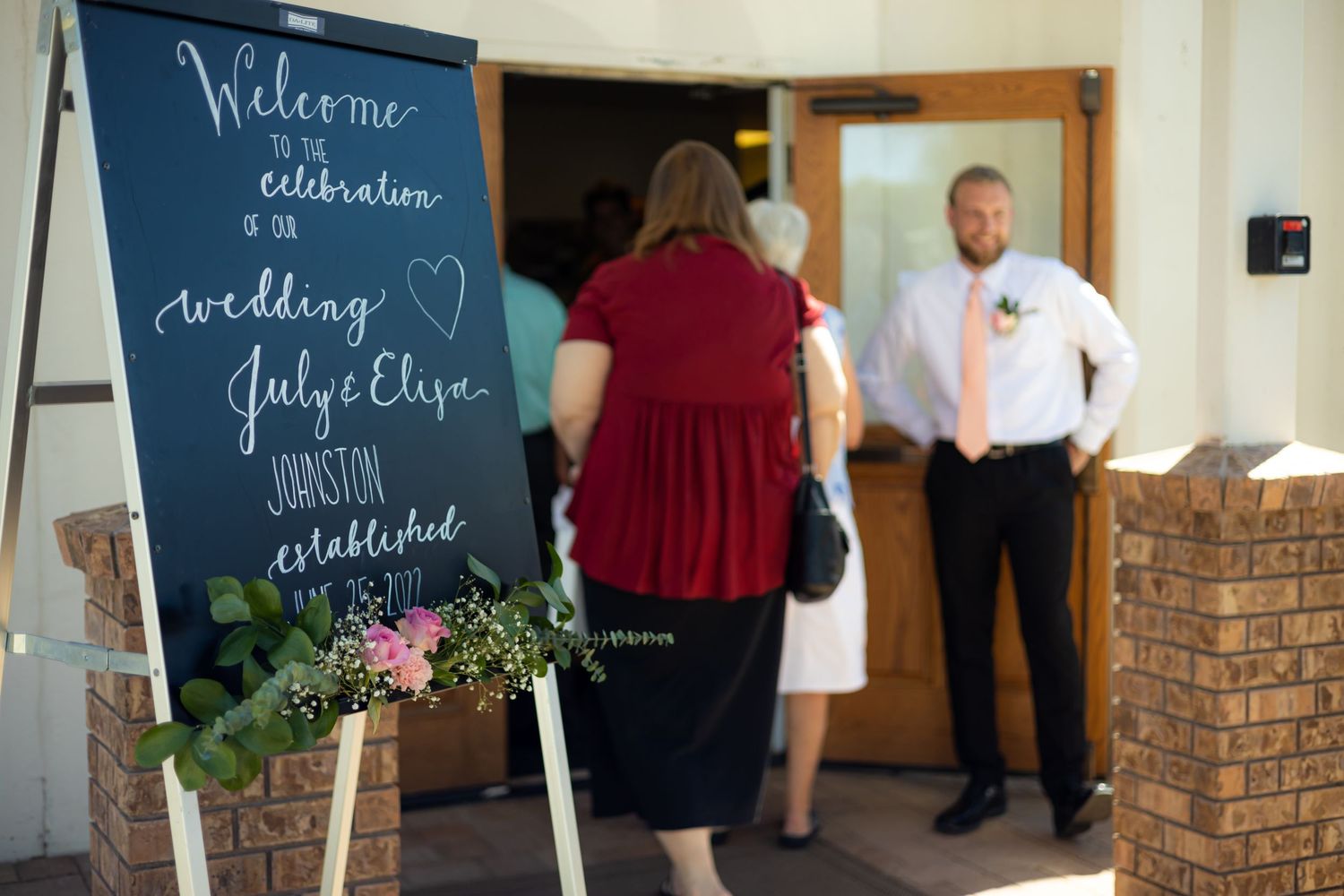 Welcome chalkboard sign with floral decorations at wedding venue entrance.