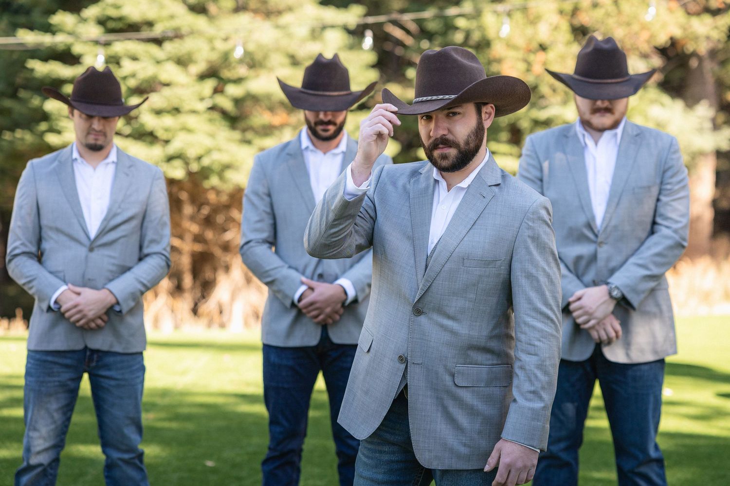Groomsmen in grey suits and cowboy hats standing together outdoors.