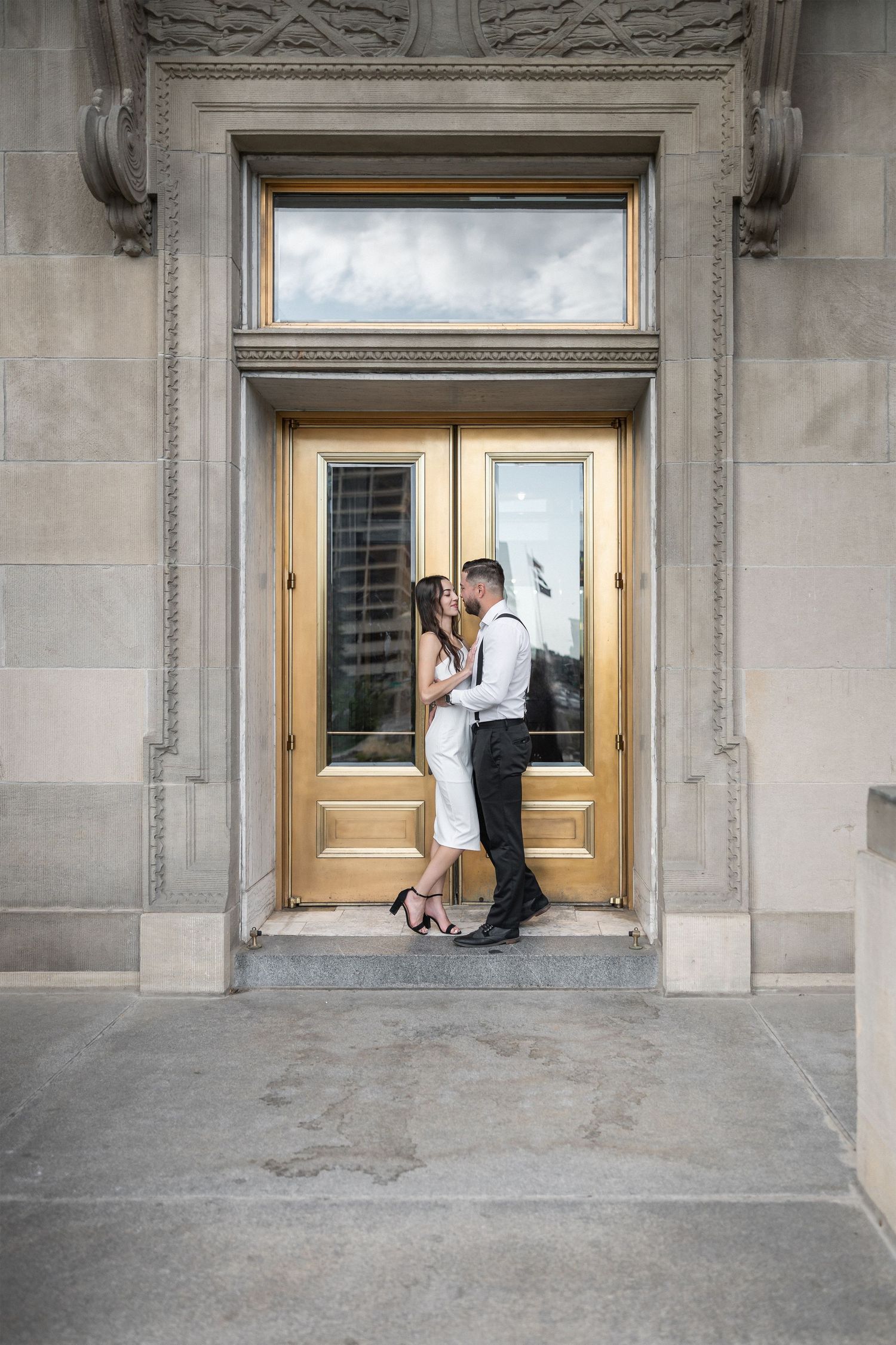 Elegant couple embraces near ornate doorway during romantic architectural photoshoot.