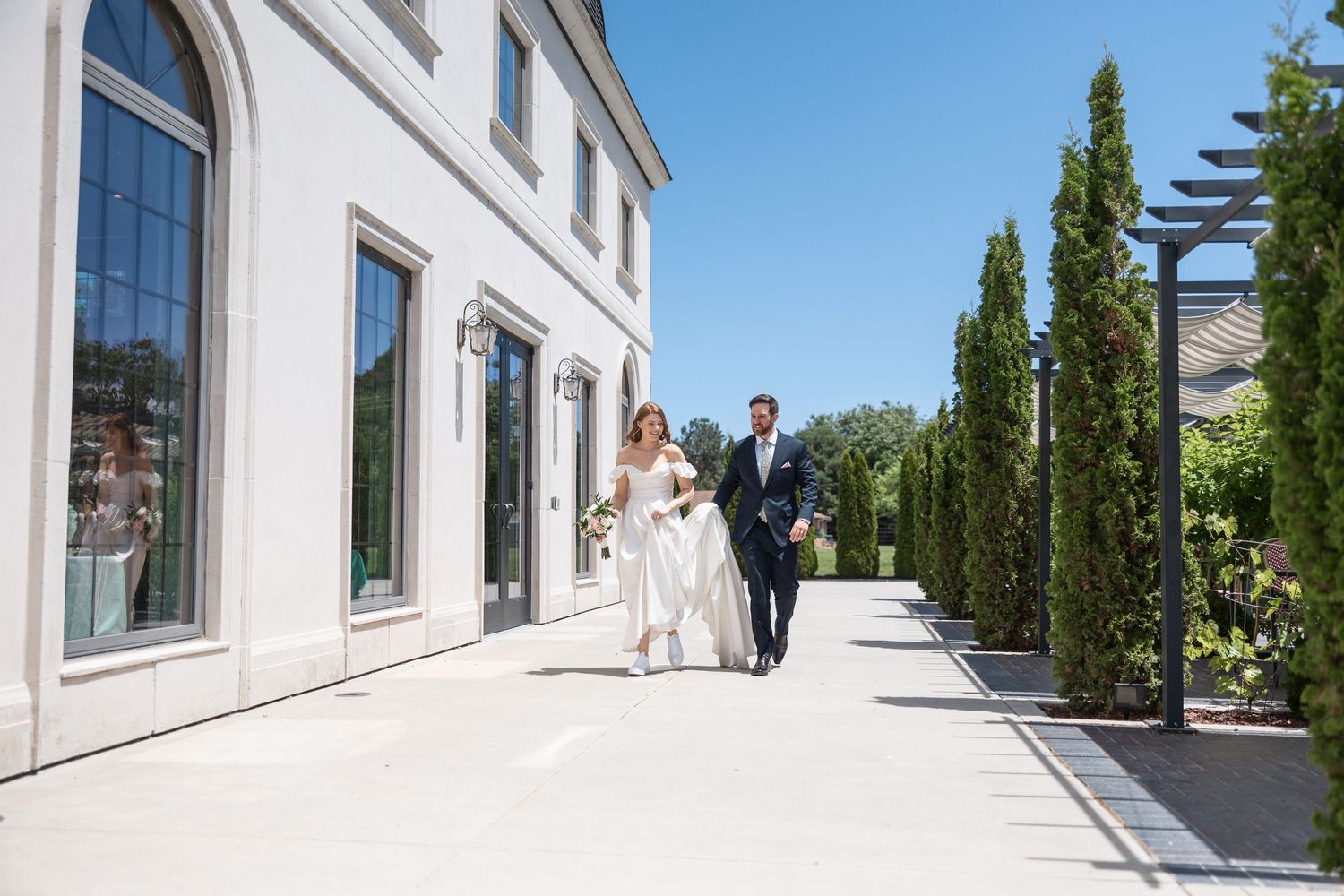 White building exterior with architectural columns and windows framing a wedding scene.