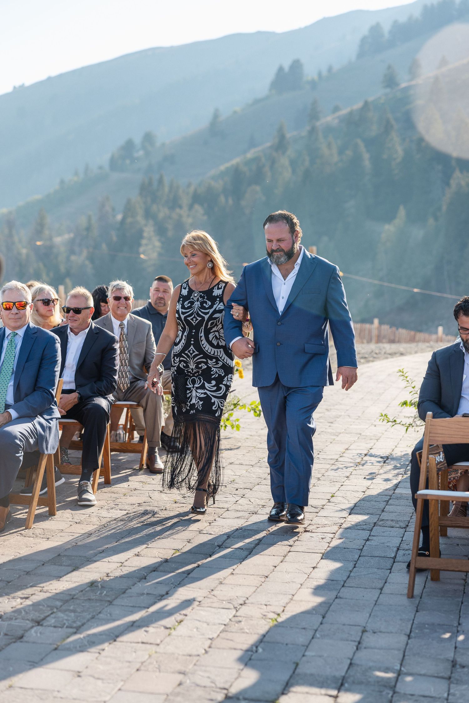 Wedding guests walk down a stone path at a mountain venue with scenic hills in the background.
