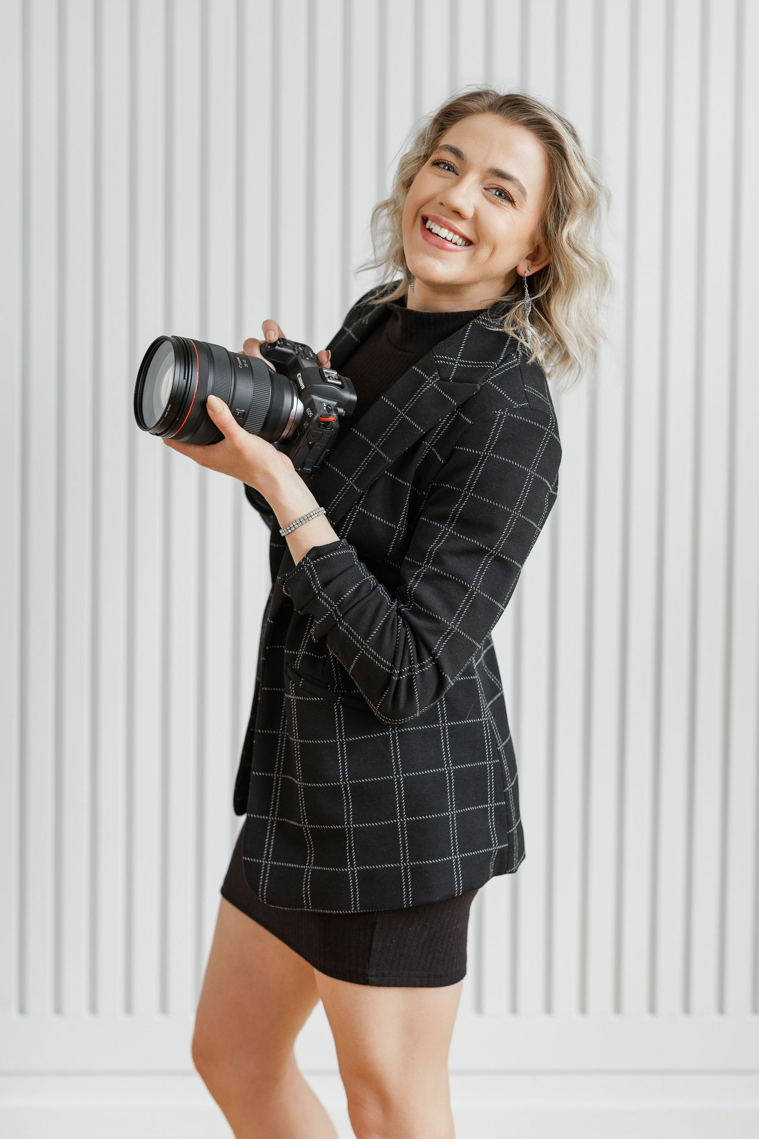 Professional photographer in black windowpane blazer poses with camera against white background in dynamic series.
