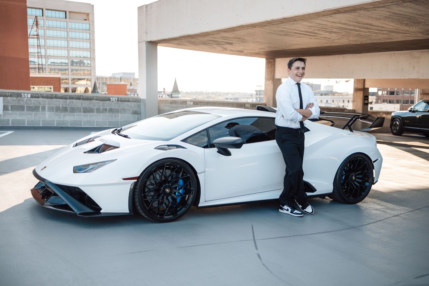White Lamborghini Aventador supercar with black wheels parked in a concrete parking garage.