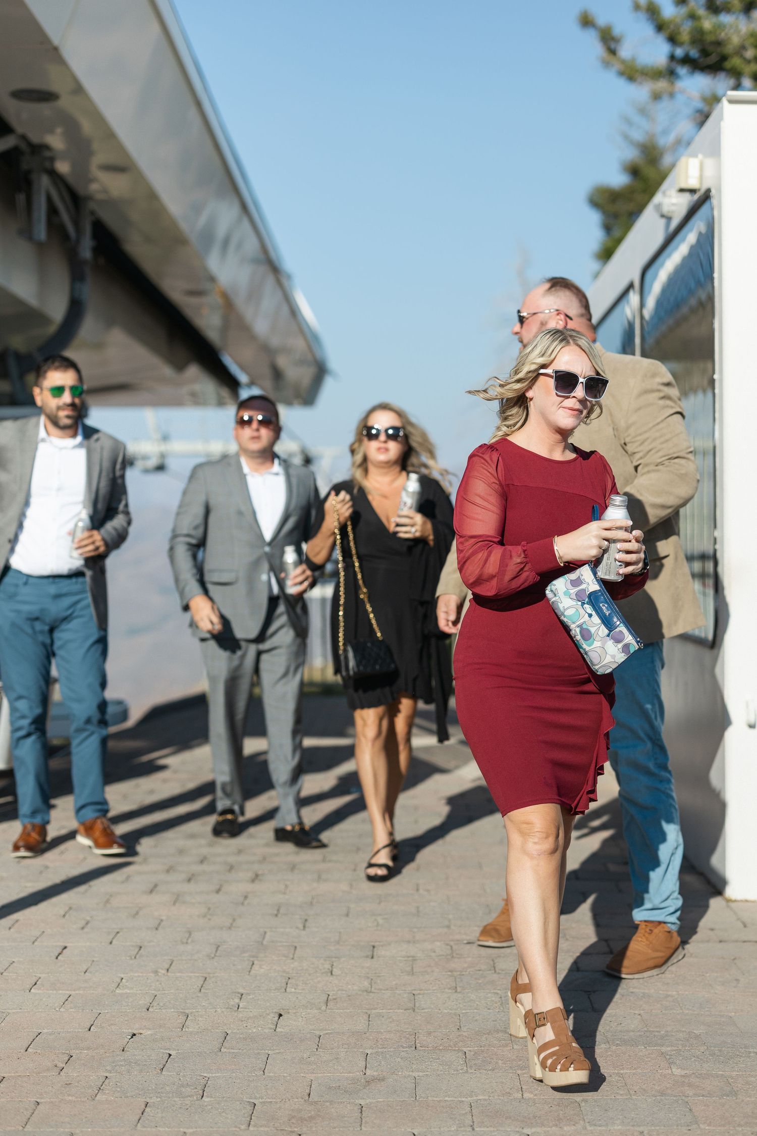 People walking along a paved pathway beneath a large overhead structure.