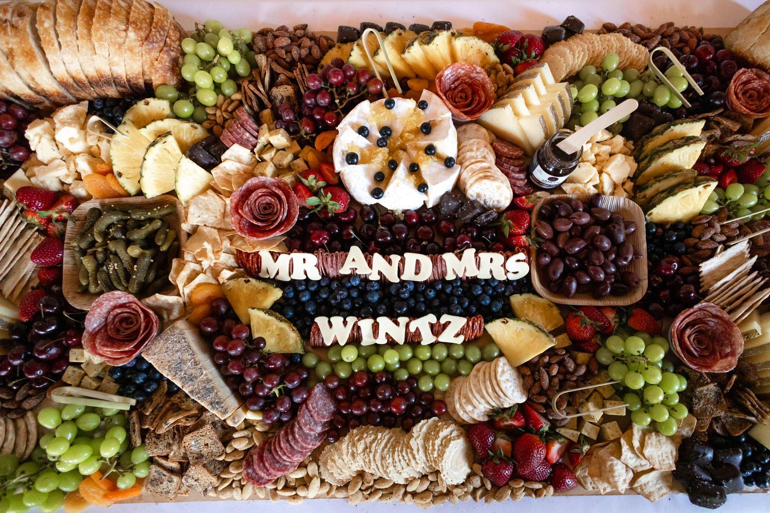 Elegant charcuterie board with 'Mr and Mrs Wintz' signage surrounded by fruits, meats and cheeses.