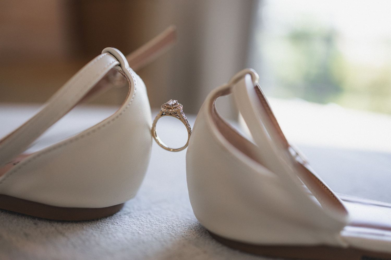 Diamond engagement ring artistically positioned between white bridal flats against natural light.