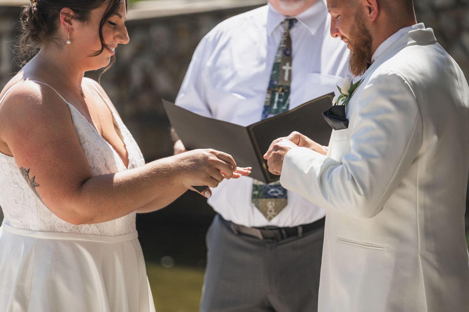 A close-up of hands exchanging wedding rings during an outdoor ceremony.