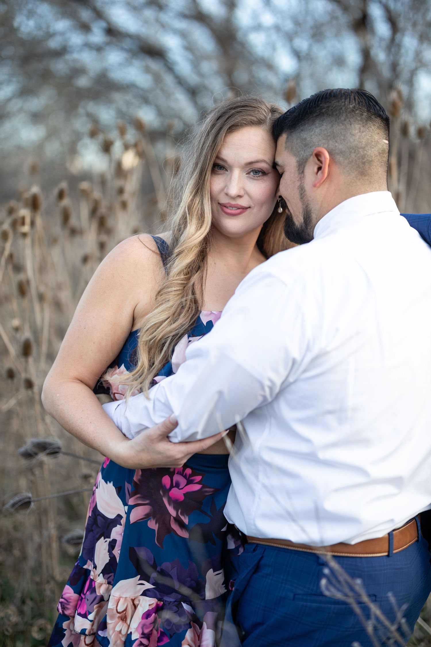 Tender moment between couple in formal wear standing among dried winter foliage.