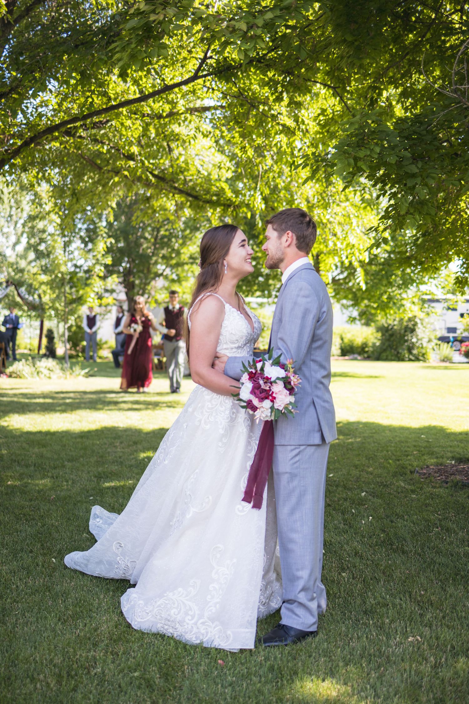 Romantic wedding portrait of couple standing together under sunlit trees.