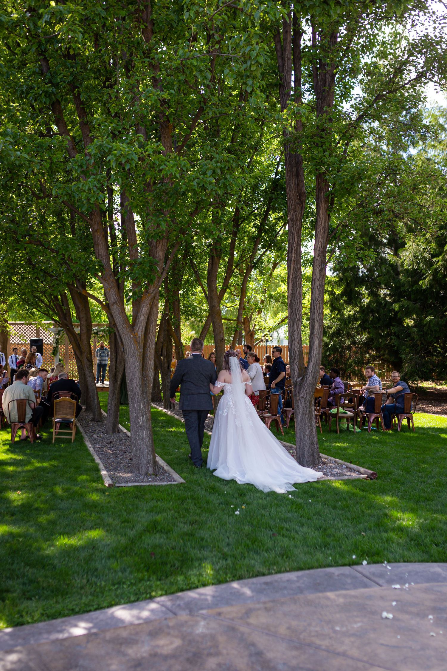 Wedding ceremony taking place in a serene wooded area with guests seated on white chairs.