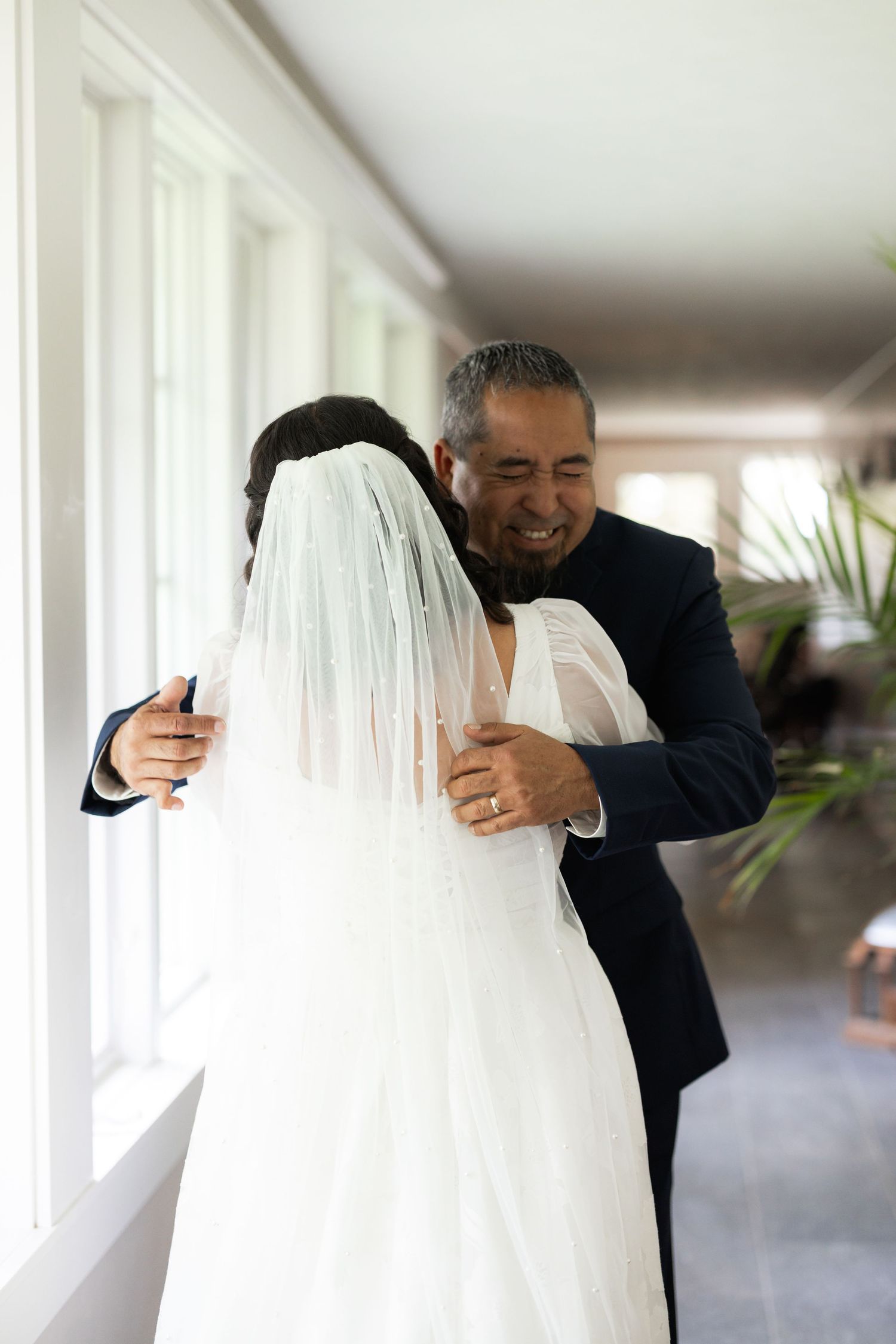 Emotional moment shared between wedding dress and formal suit in hallway.