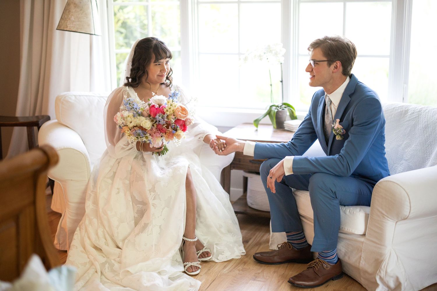 A couple shares an intimate moment on white sofa during their wedding celebration.