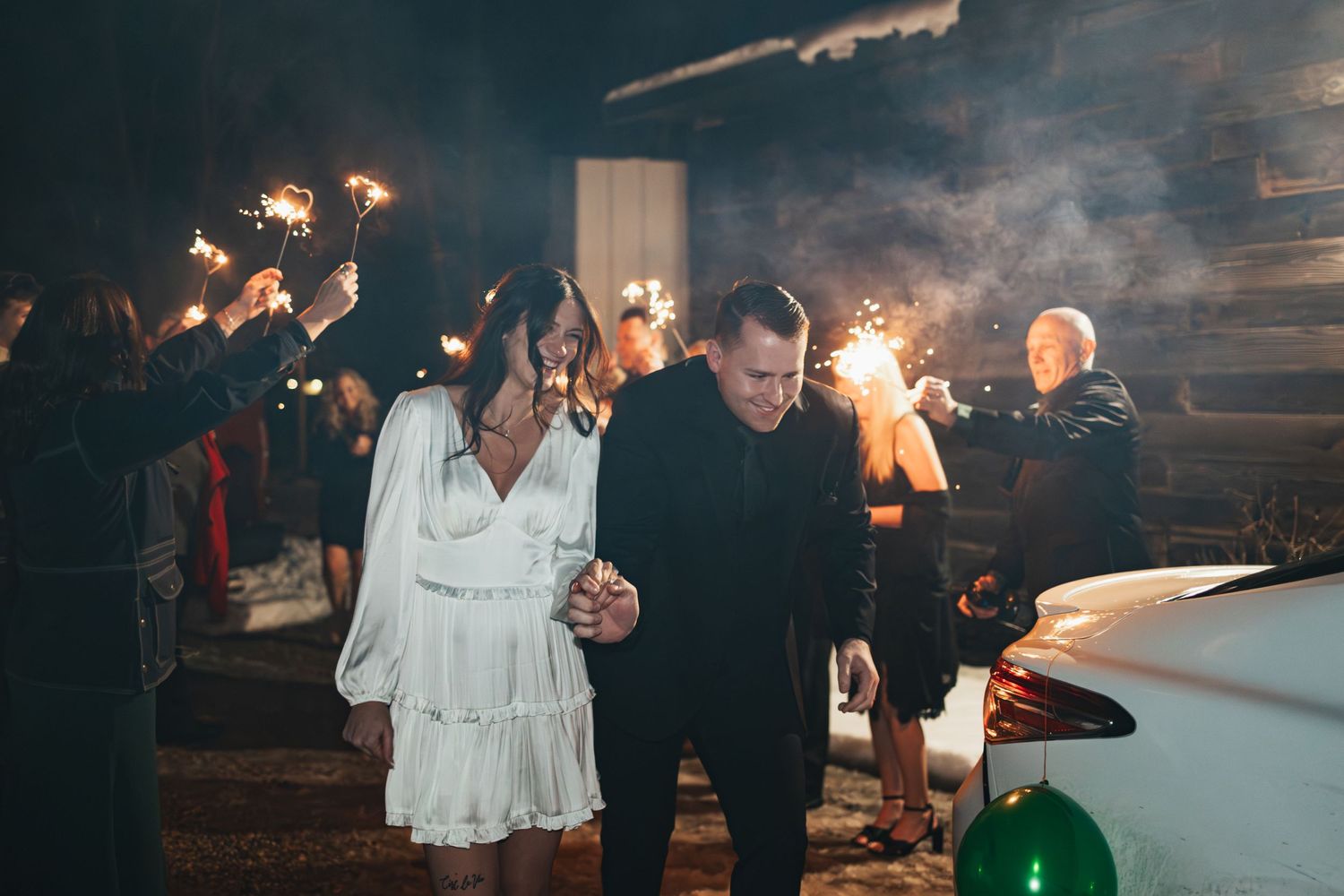 Couple walks through a sparkler-lit path during their nighttime wedding celebration.
