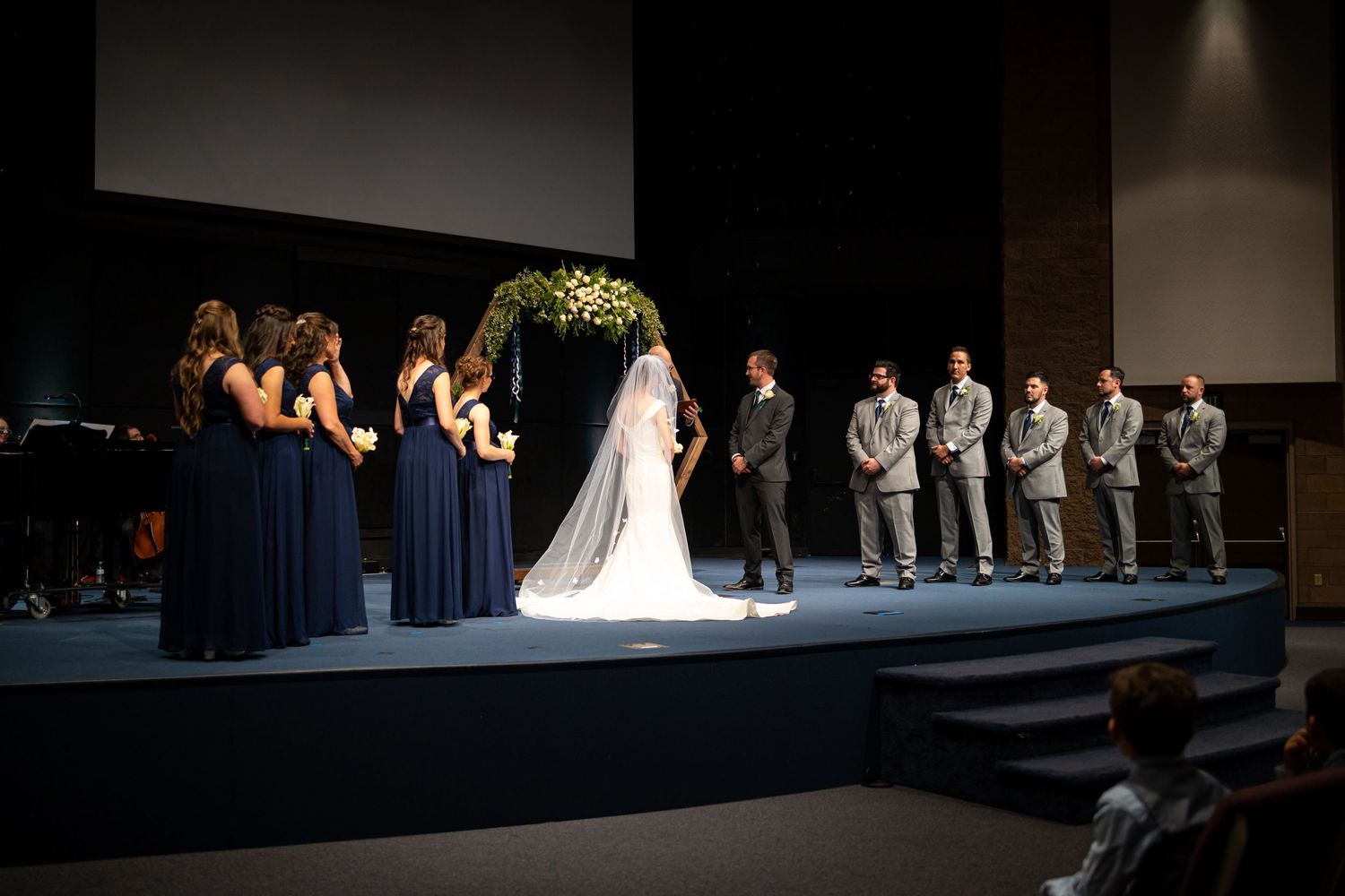 Wedding party arranged on stage under dramatic spotlights during ceremony.