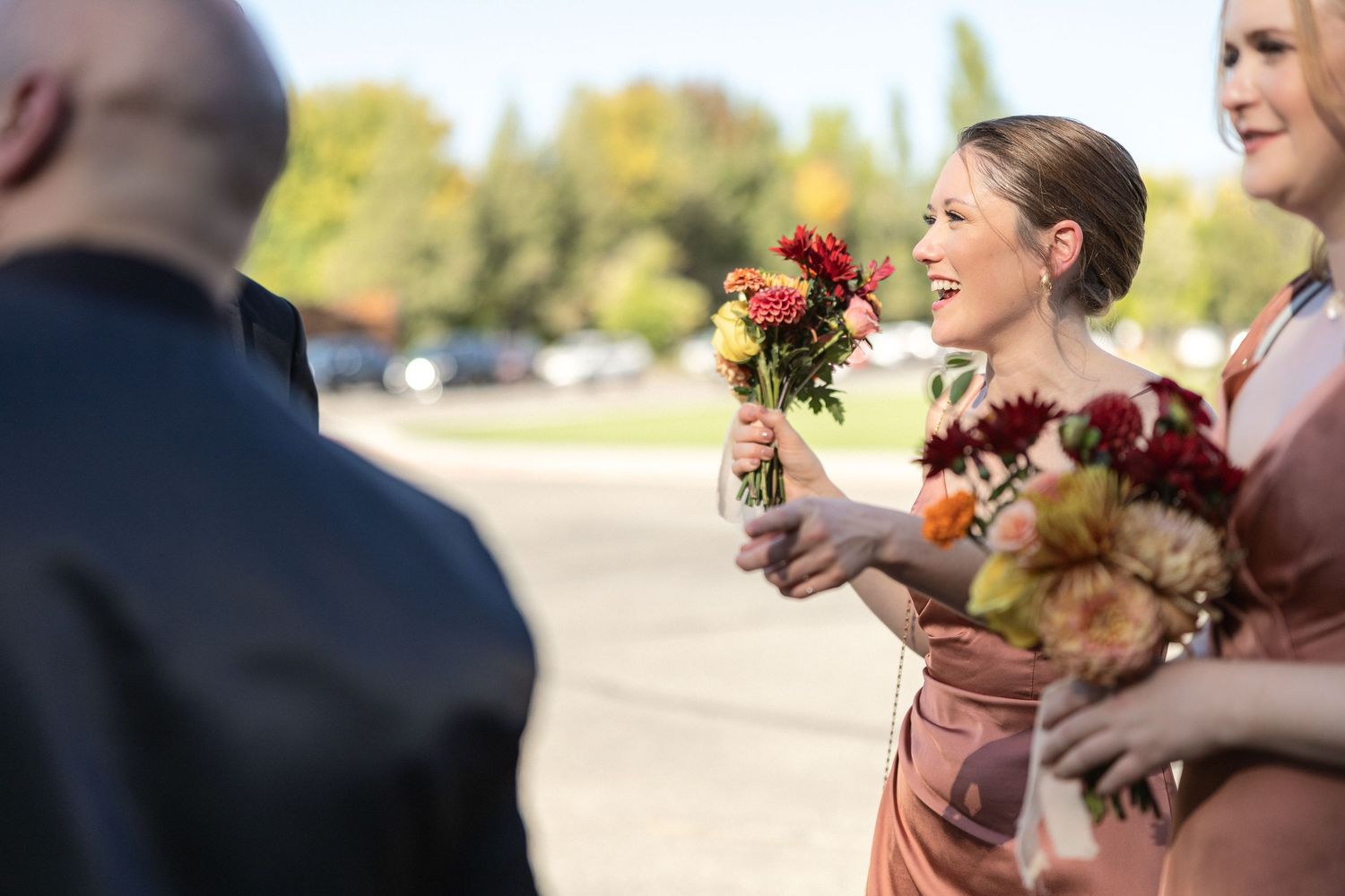 Wedding party members hold colorful fall bouquets during an outdoor ceremony.