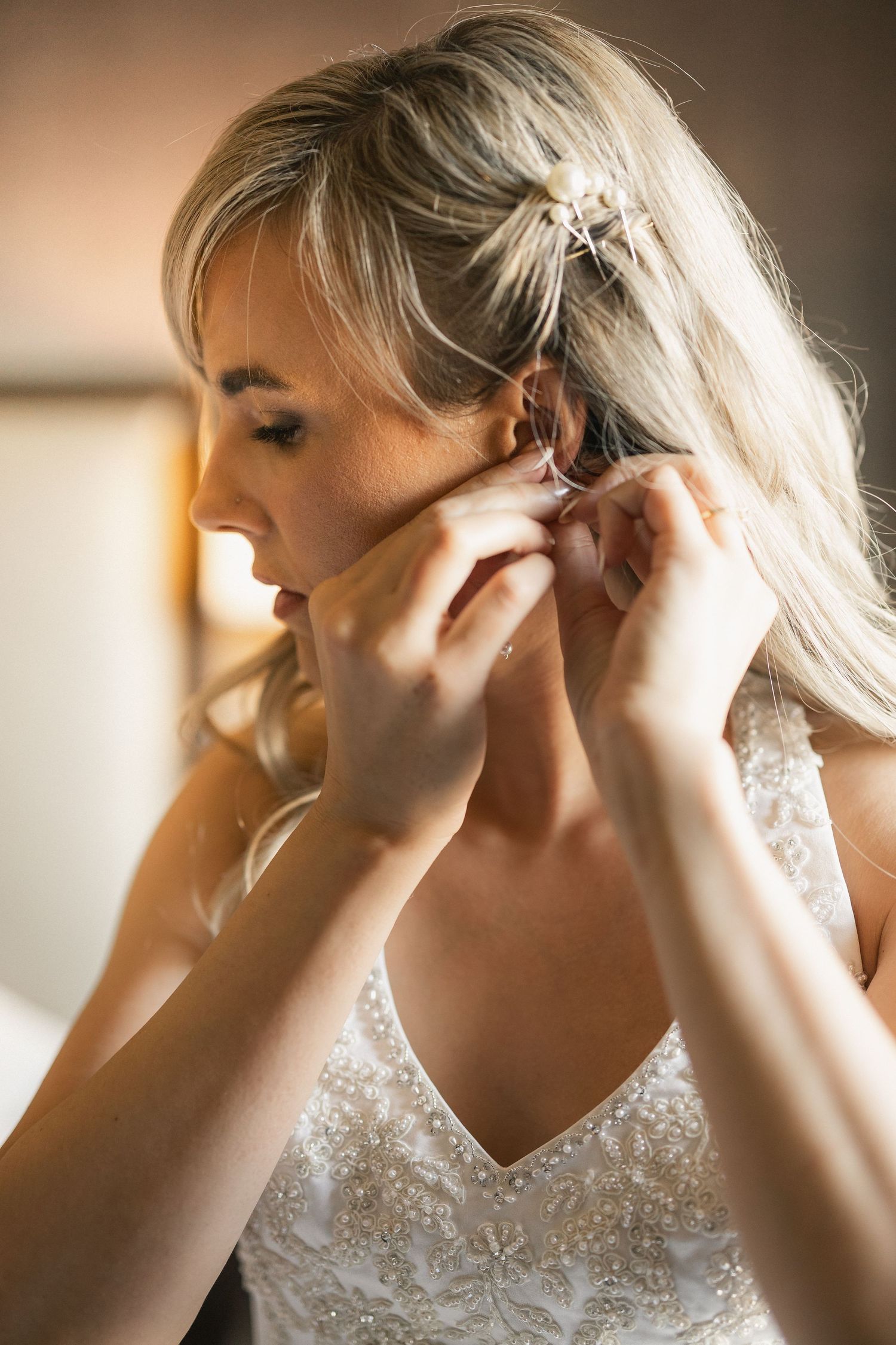 Close-up of a bride putting on elegant earrings while wearing a lace wedding dress.