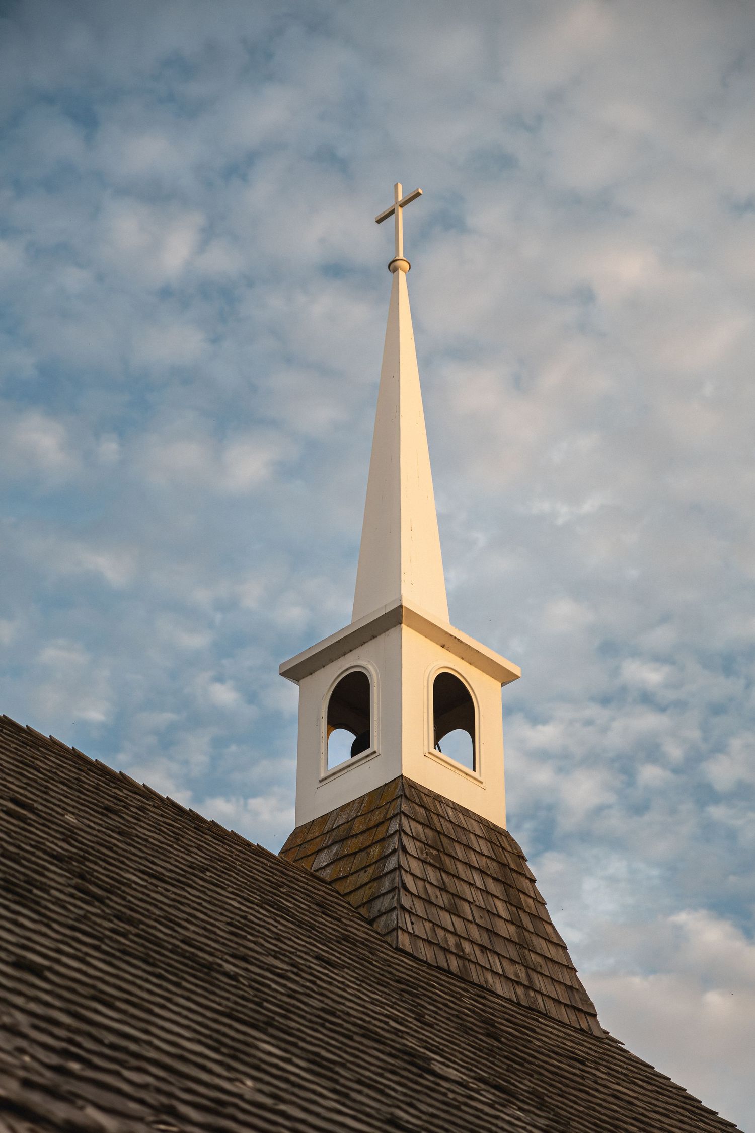White church steeple with cross rises against cloudy blue sky.