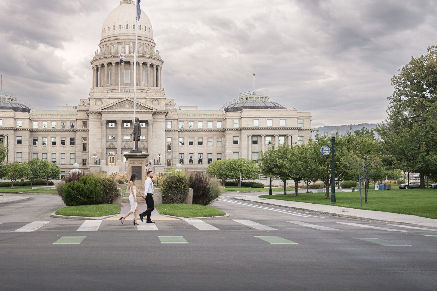 Wide view of a state capitol building with manicured grounds and cloudy sky.