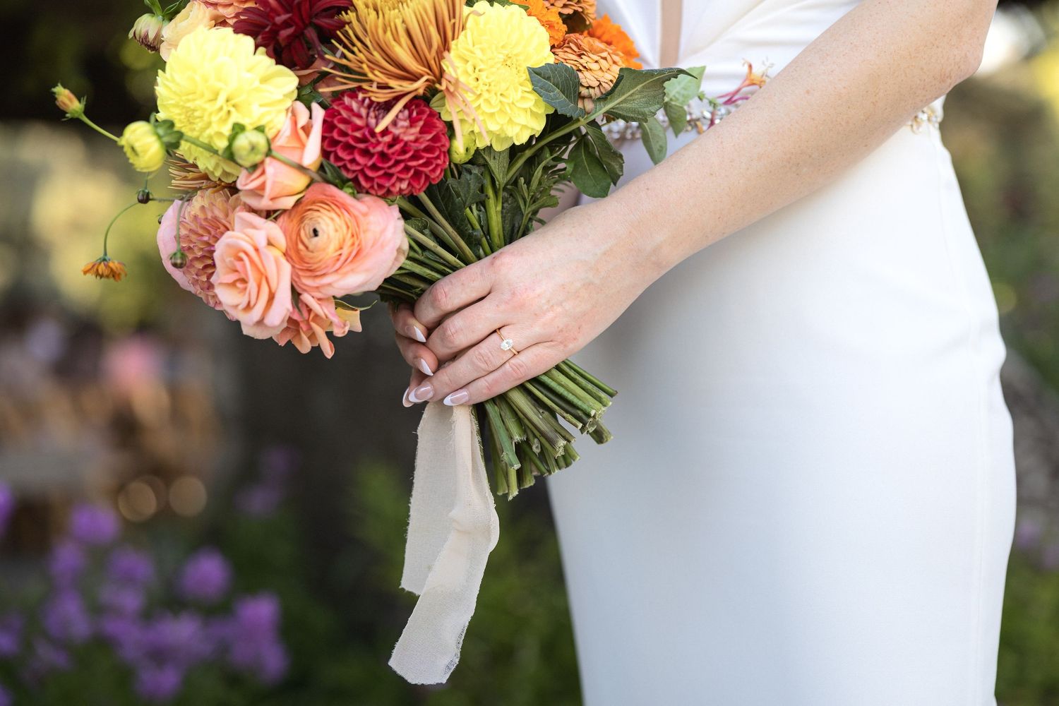 Beautiful wedding bouquet with pink and peach roses against a white dress background.