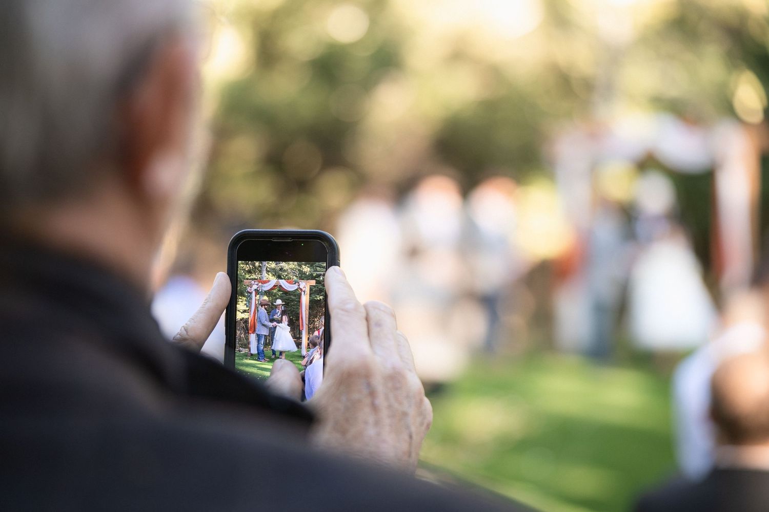Guest capturing wedding ceremony on smartphone from audience perspective.
