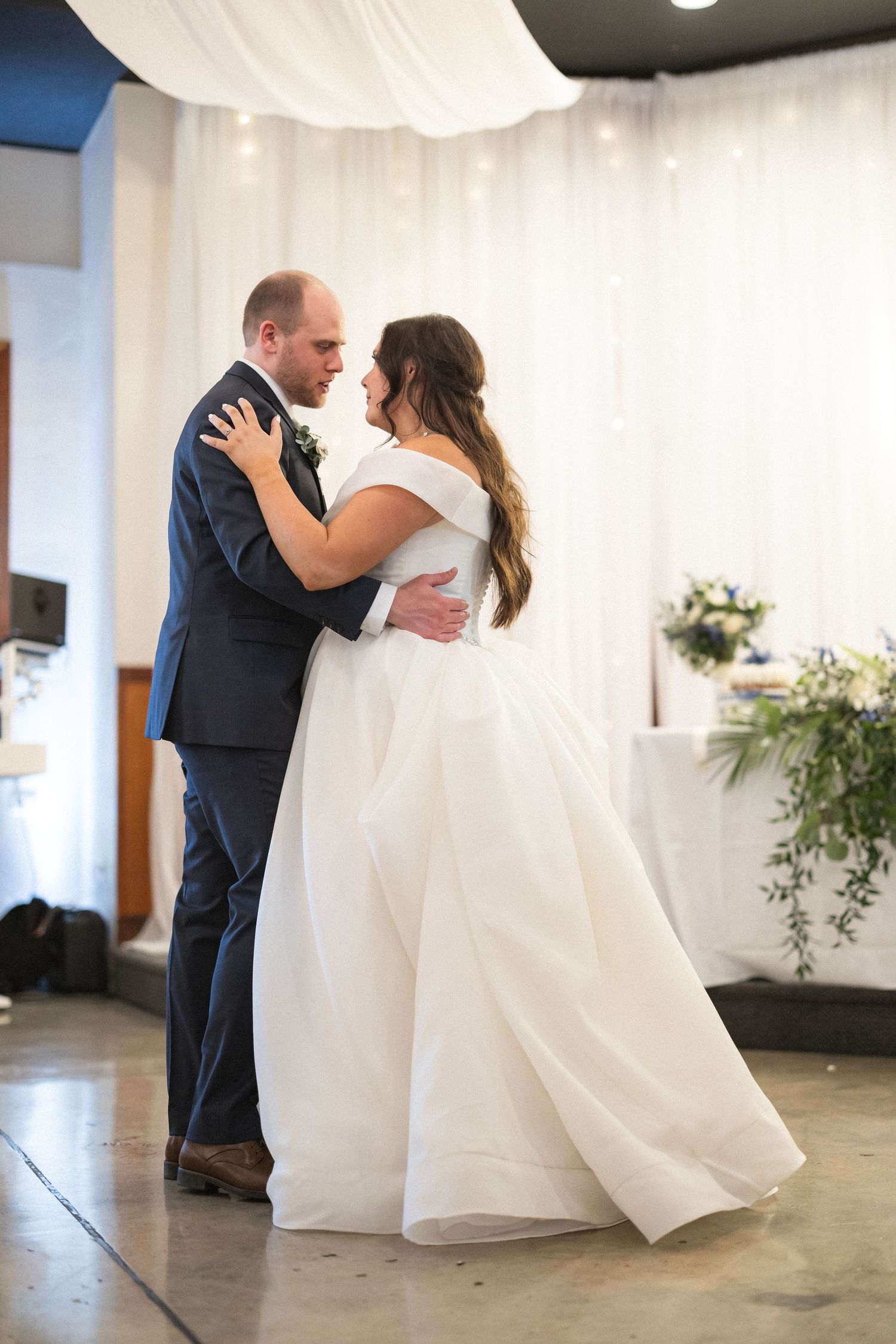 A tender dance moment at a wedding reception with white draping and floral decor in the background.