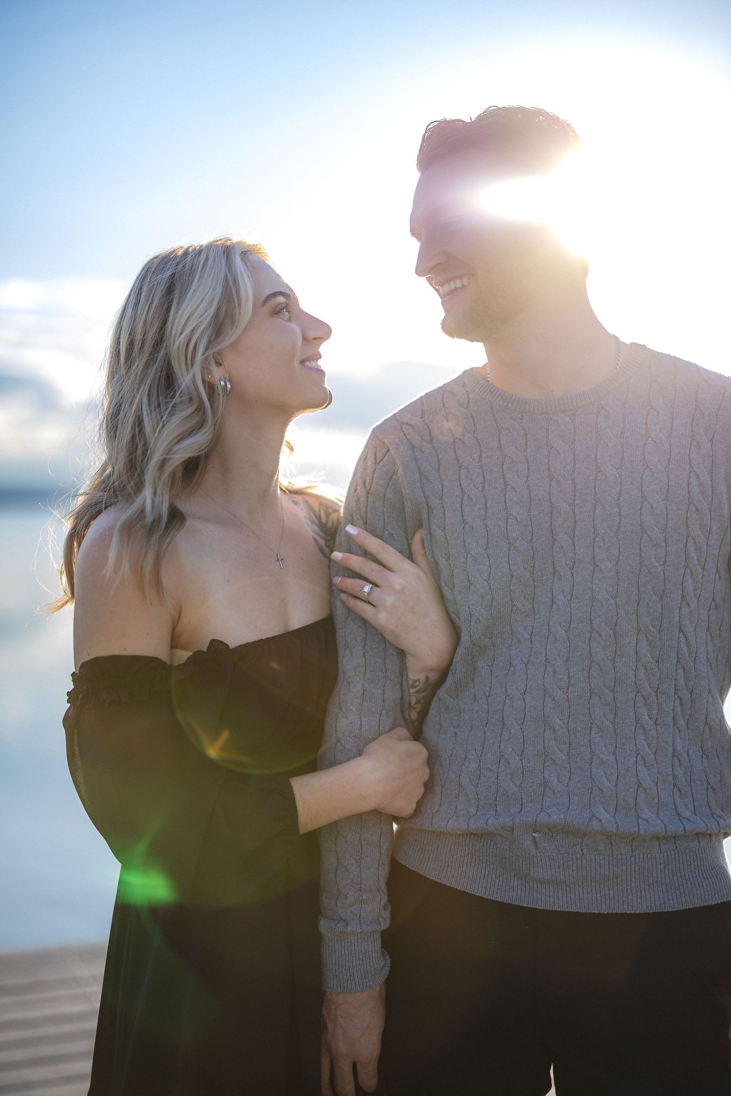 A couple shares an intimate moment on a dock with sunlight flaring behind them.