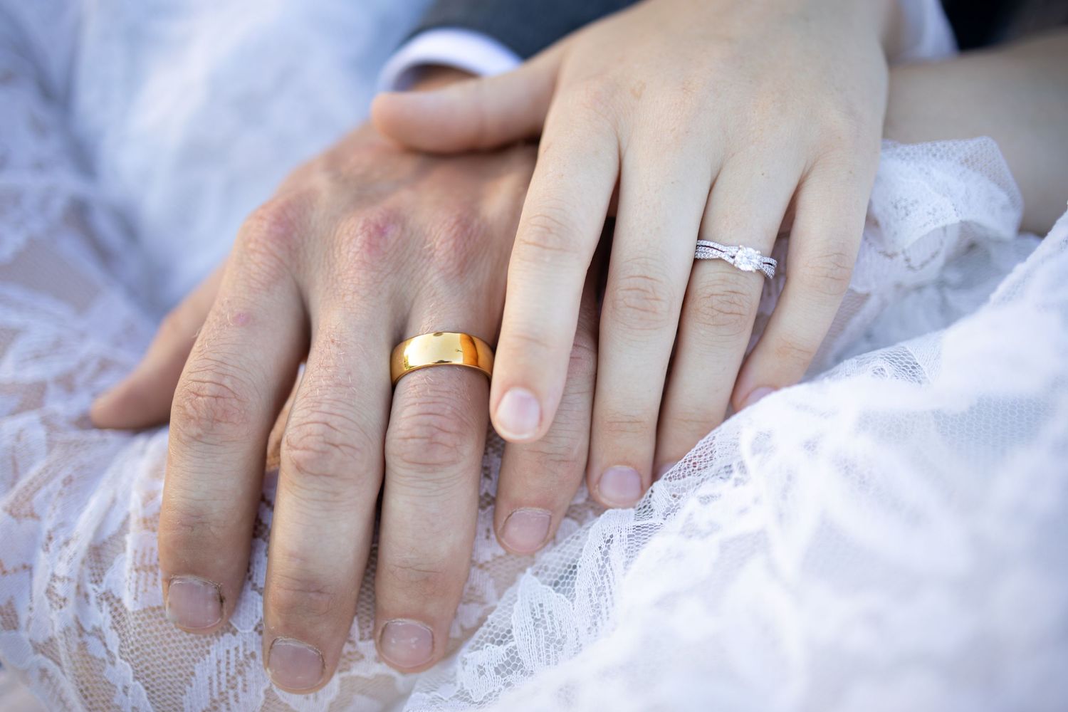 Close up shot of hands with wedding rings on white lace fabric showing gold and diamond bands.