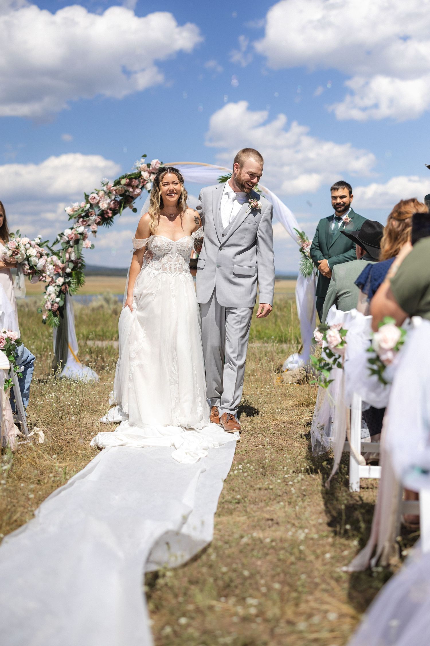 Newlyweds walking down white aisle runner at outdoor mountain wedding ceremony.